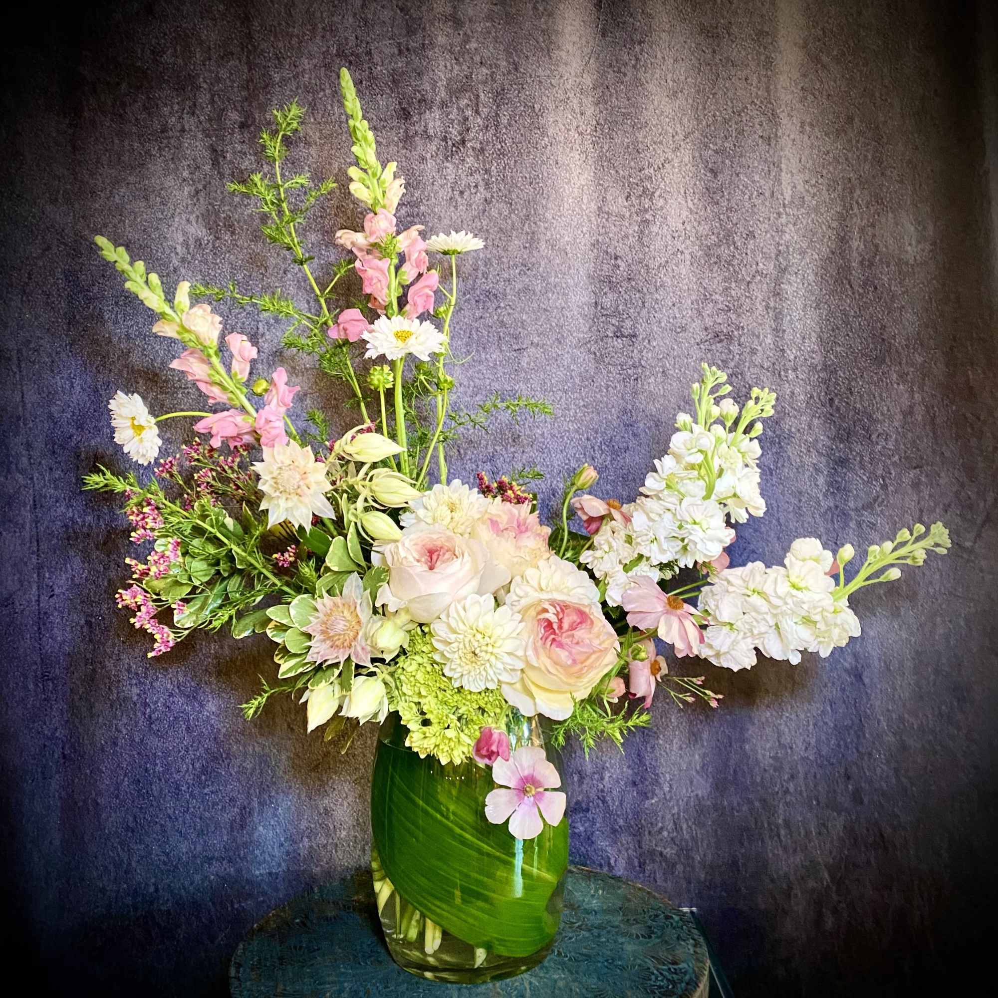 Pink and white floral arrangement in a green glass vase