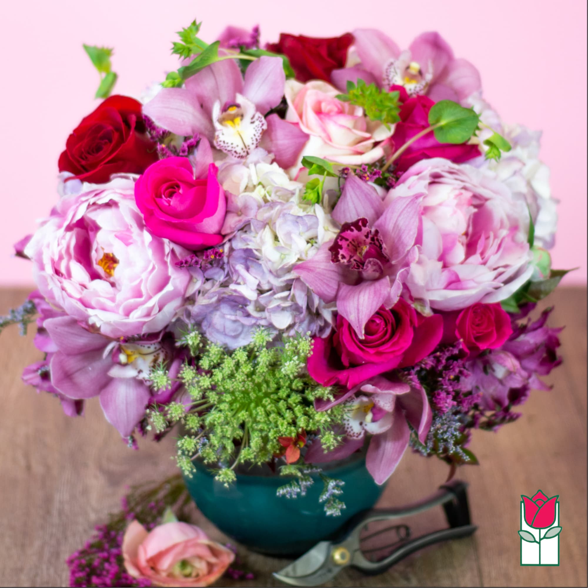 Pink and red bouquet with roses, peonies, and orchids in a teal vase