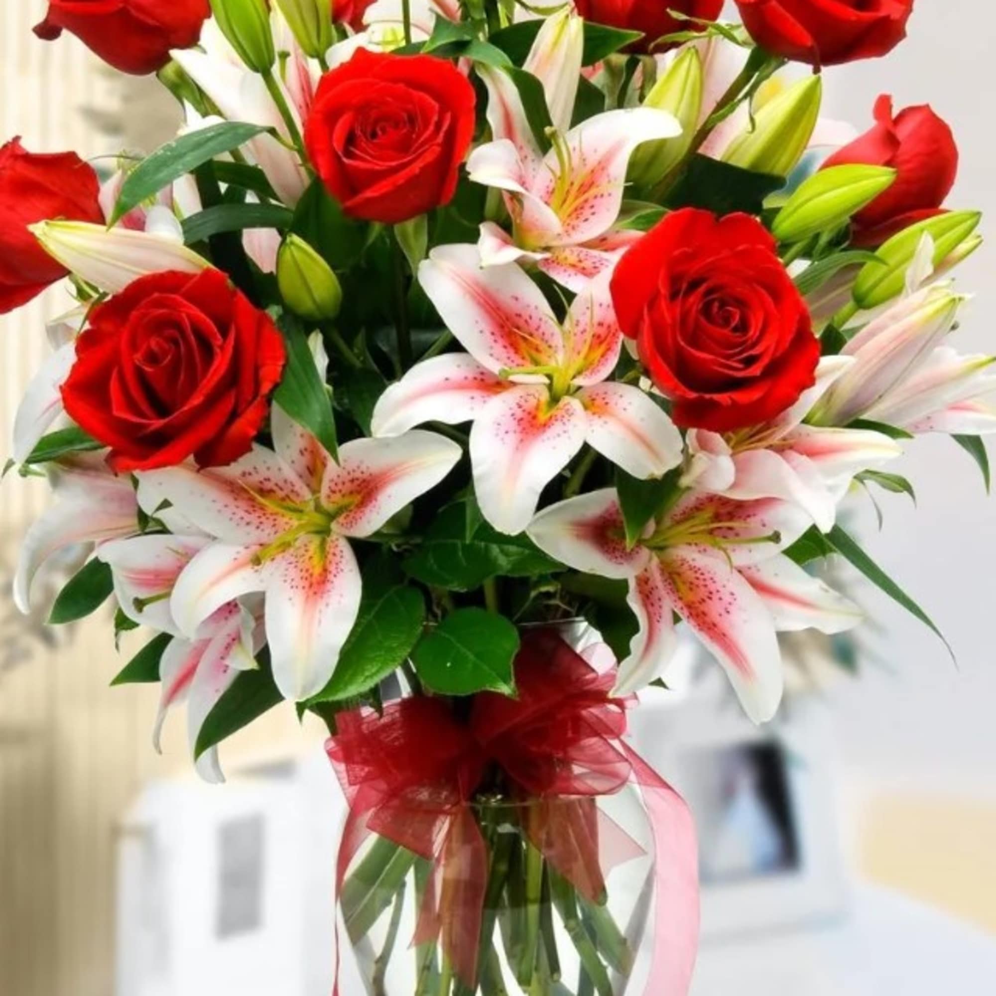 Red roses and white lilies in a clear glass vase with a red ribbon
