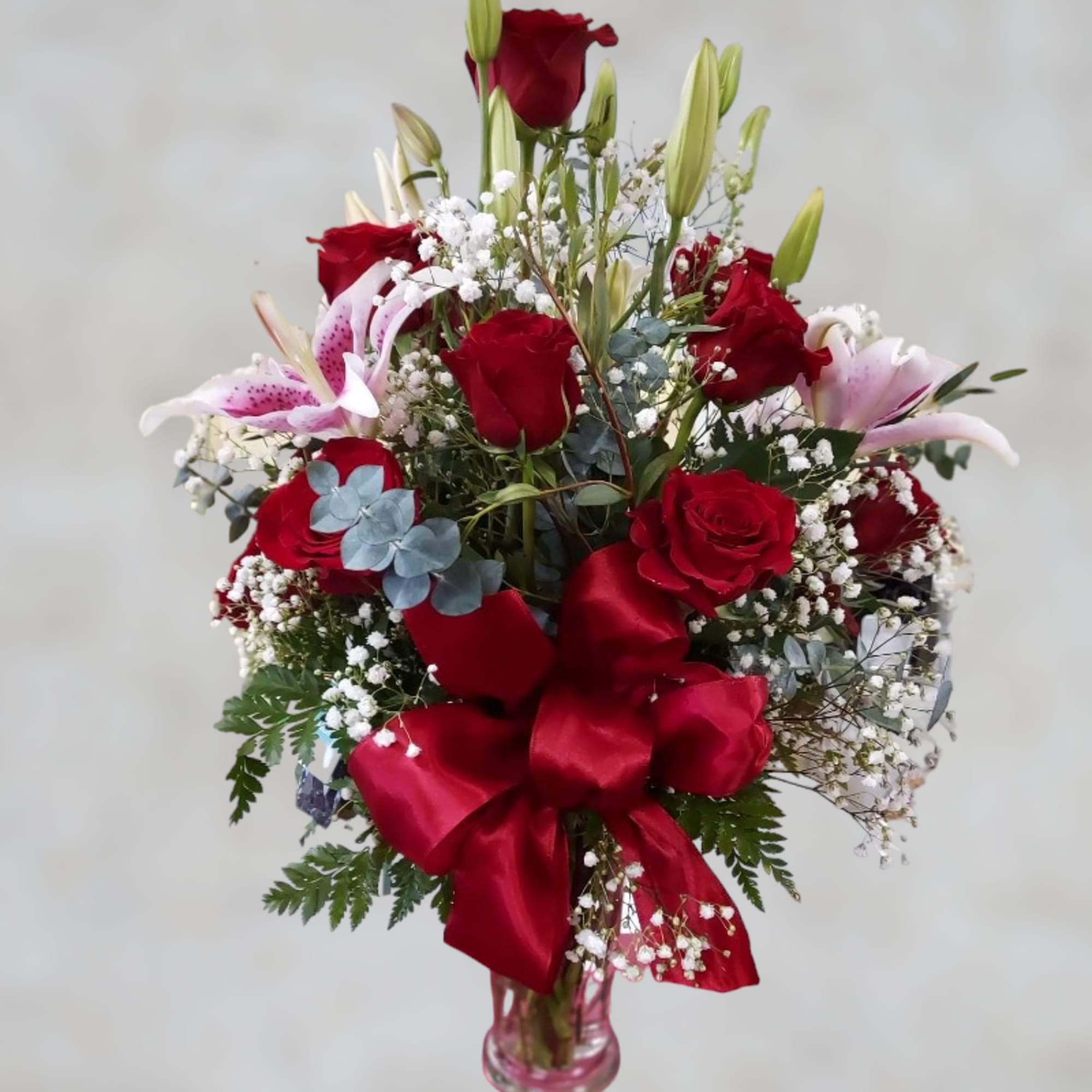 Red roses and pink lilies in a glass vase with a red ribbon