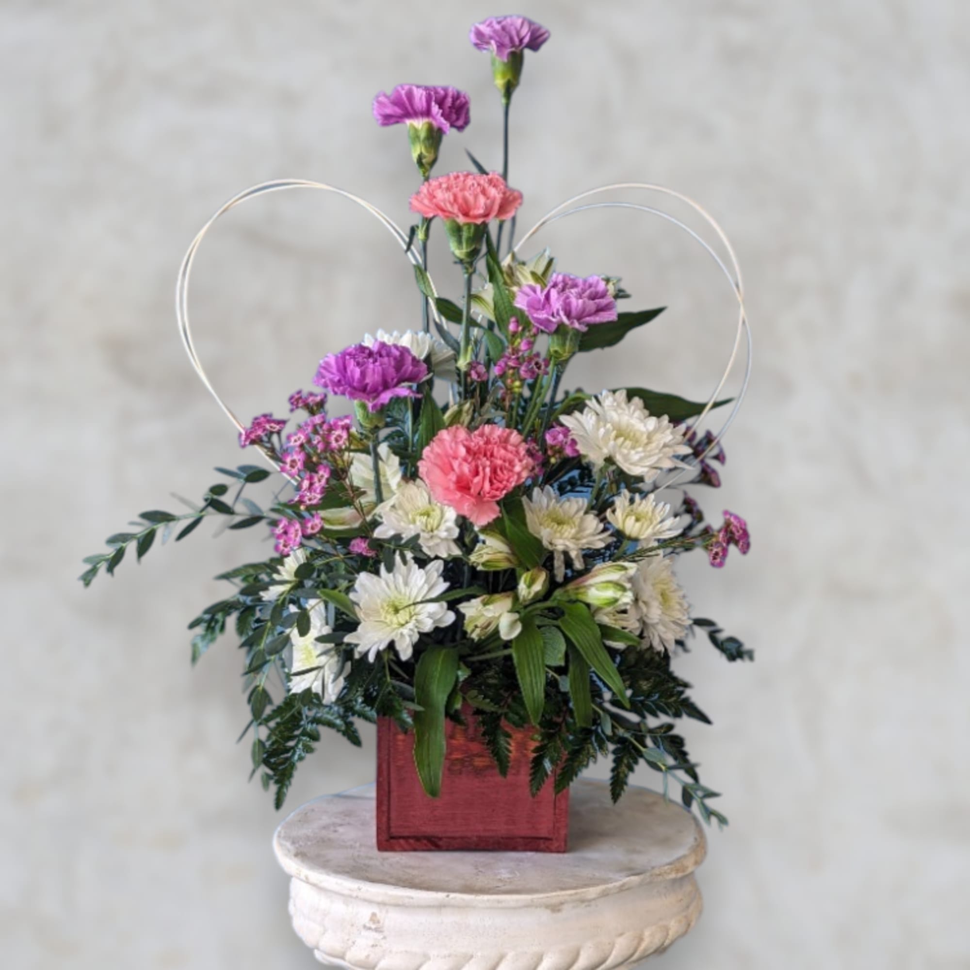 Mixed pink, purple, and white flowers in a red square container with heart loops