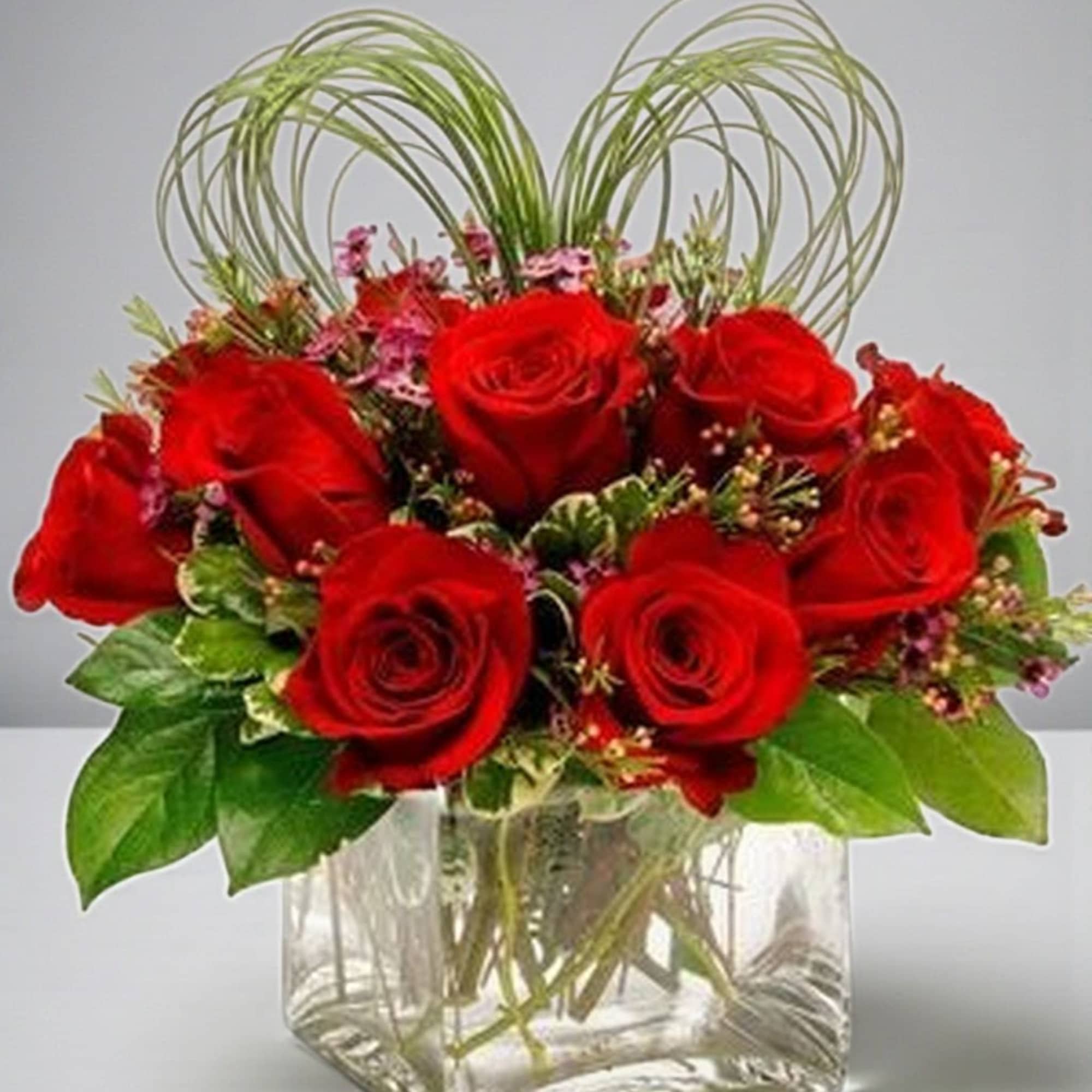 Red roses arranged in a clear square vase with looping green accents
