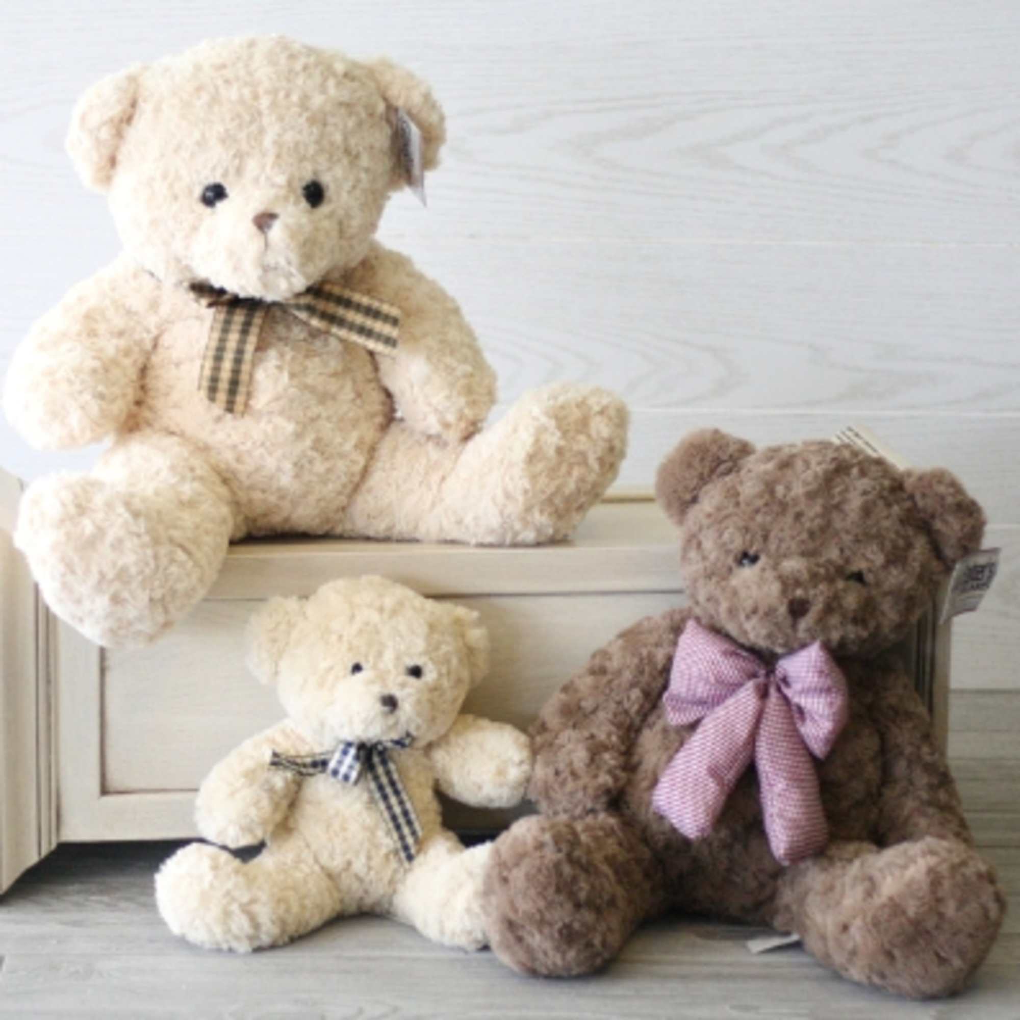 Three teddy bears with ribbon bows arranged on a wooden crate