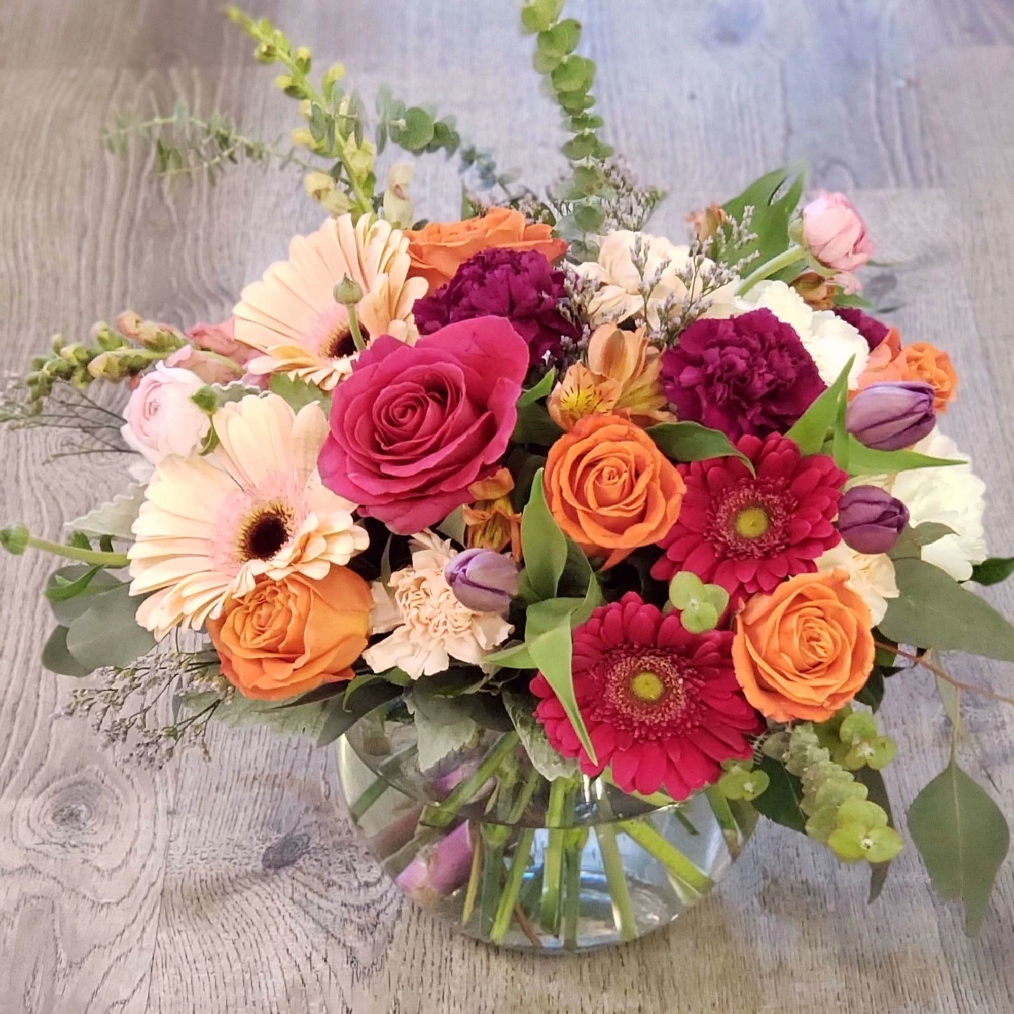 Mixed bouquet of roses, gerbera daisies, and carnations in a glass vase