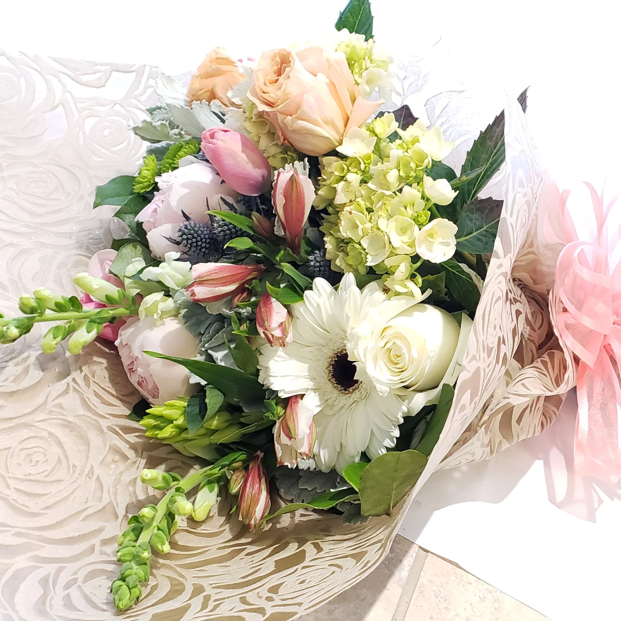 Bouquet of white and blush flowers wrapped in patterned paper with a pink ribbon