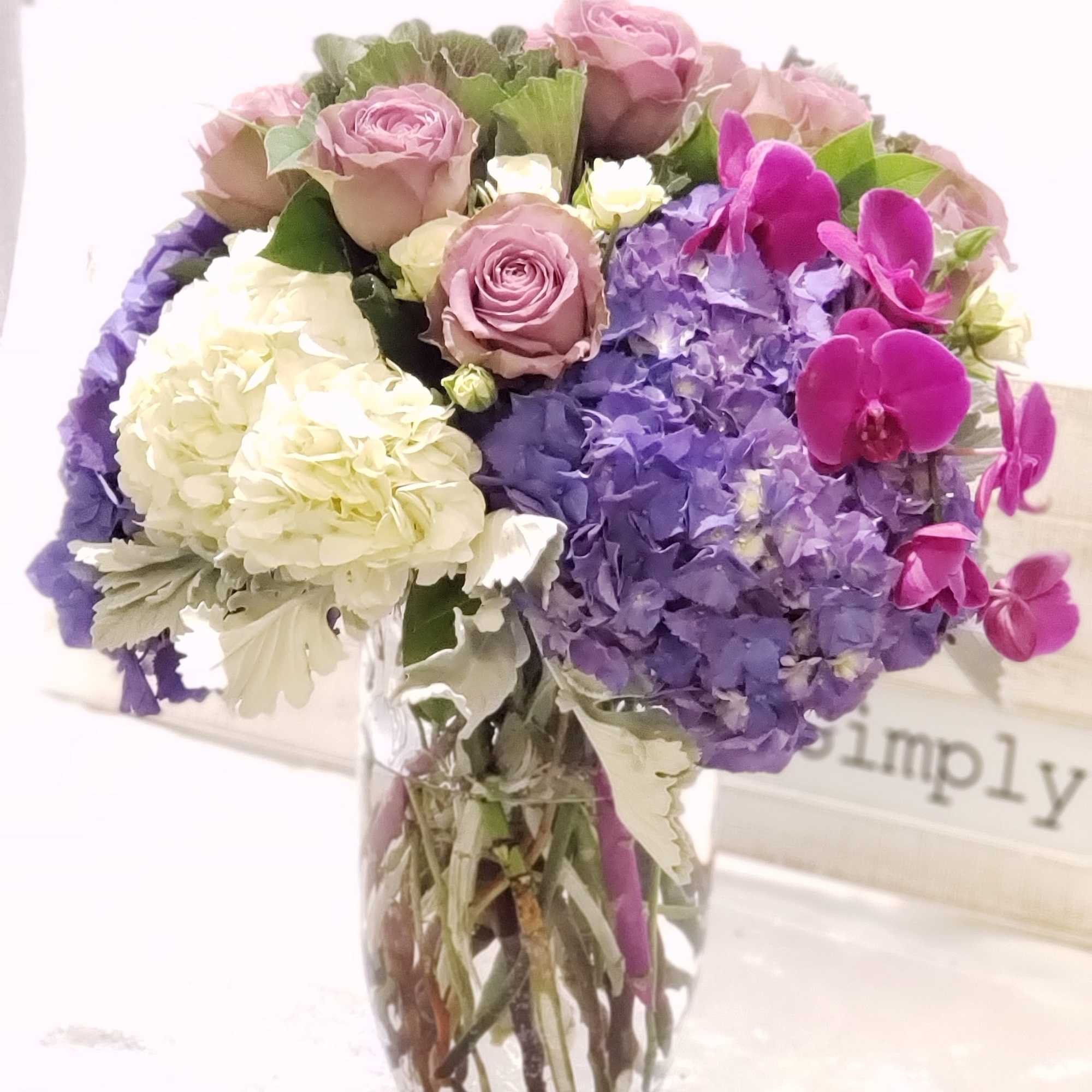 Bouquet of pink roses, purple hydrangeas, and magenta orchids in a glass vase