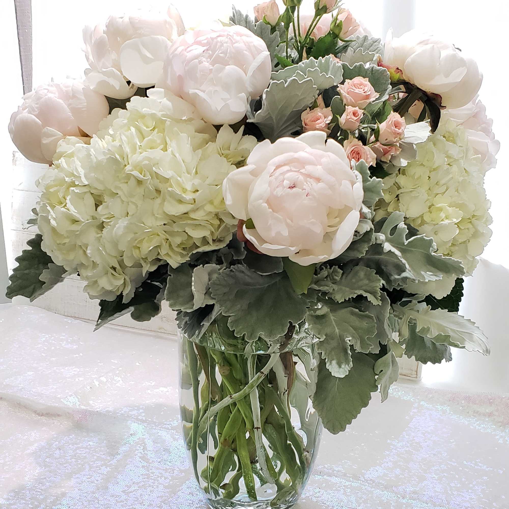 Blush peonies and pale hydrangeas in a clear glass vase
