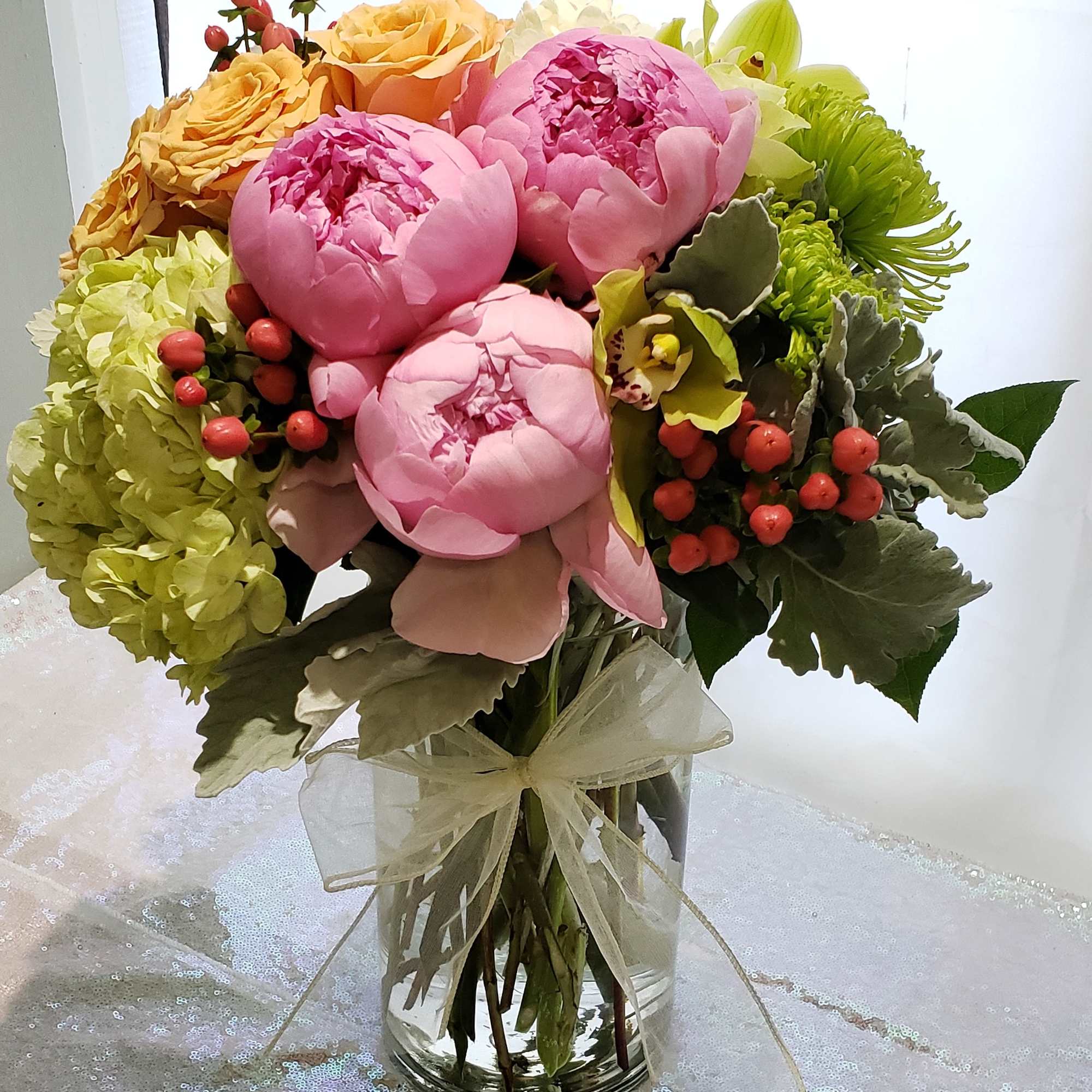 Bouquet of pink peonies, yellow roses, and green hydrangeas in a glass vase