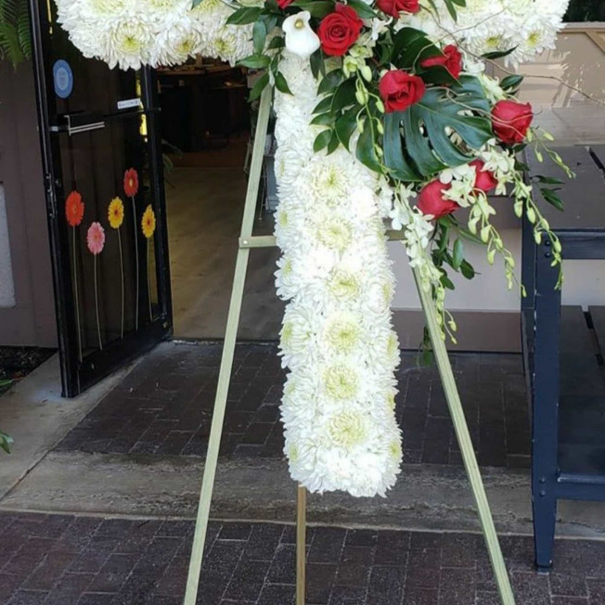 Standing floral cross with white chrysanthemums and red roses on an easel