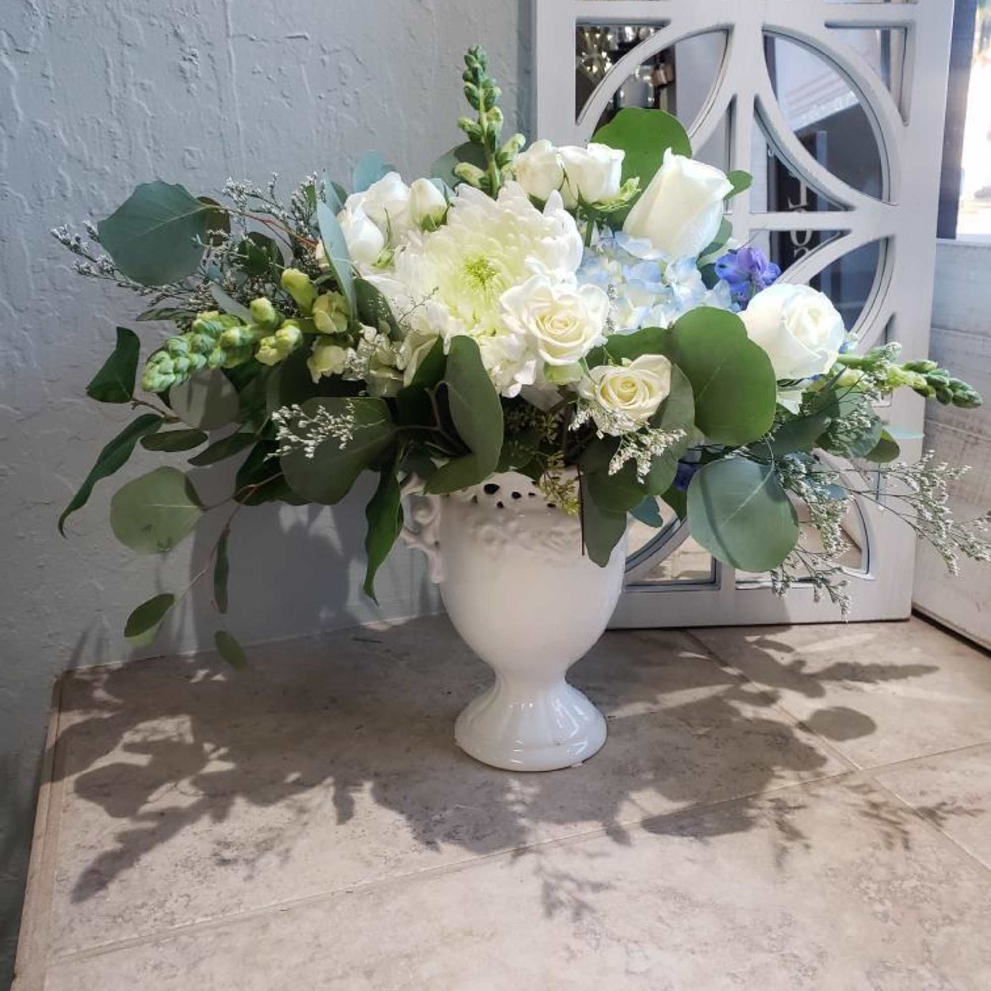 White floral arrangement in a white urn vase with greenery