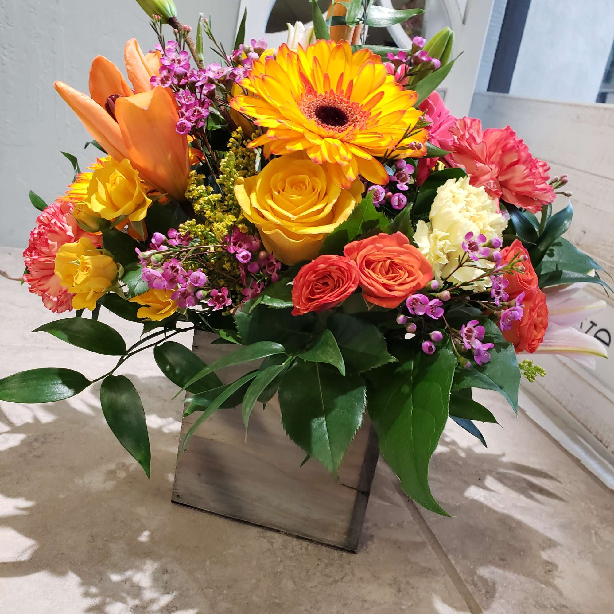 Bright mixed bouquet with gerbera daisies, roses, lilies, and carnations in a wooden box