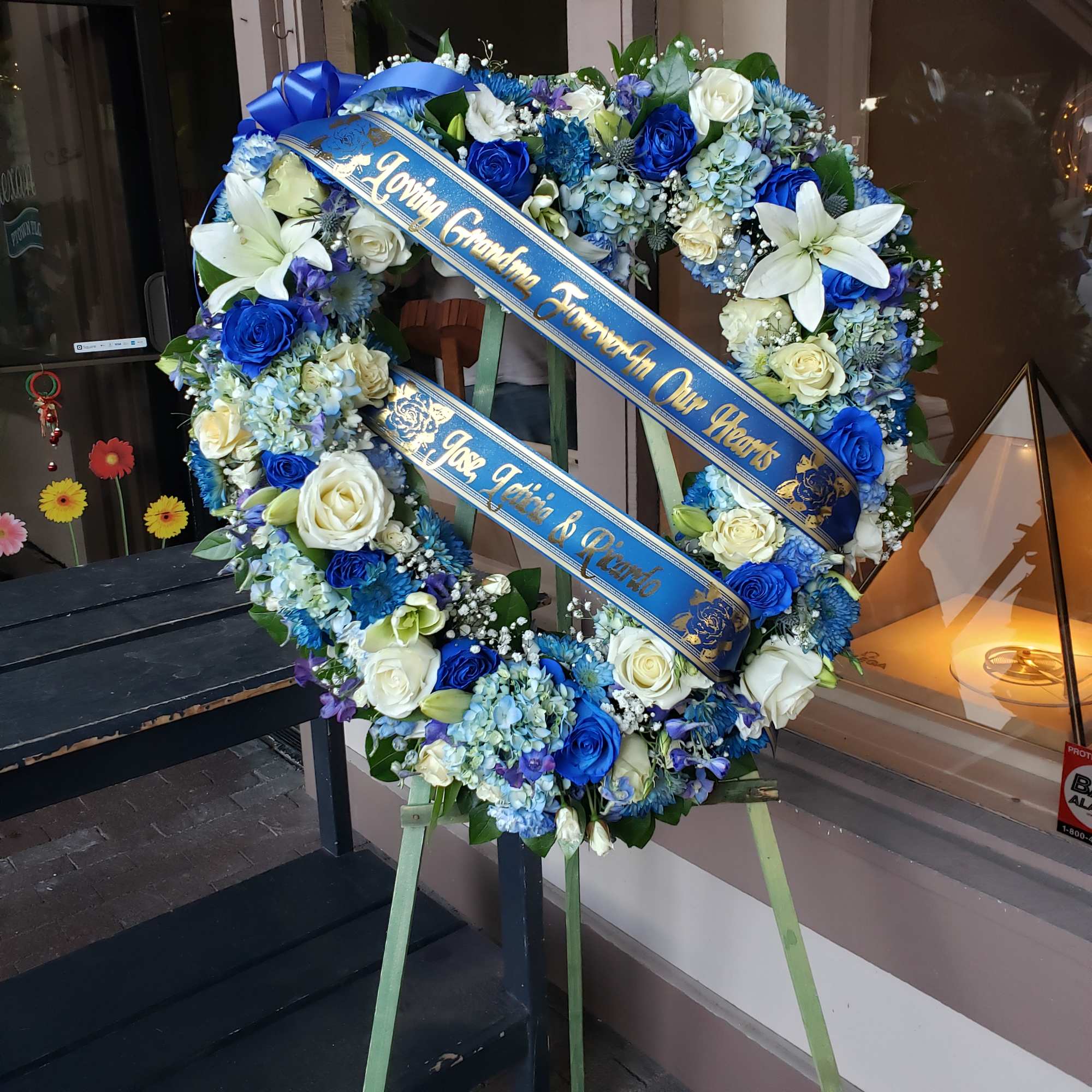 Blue and white floral funeral wreath on an easel with ribbon banners