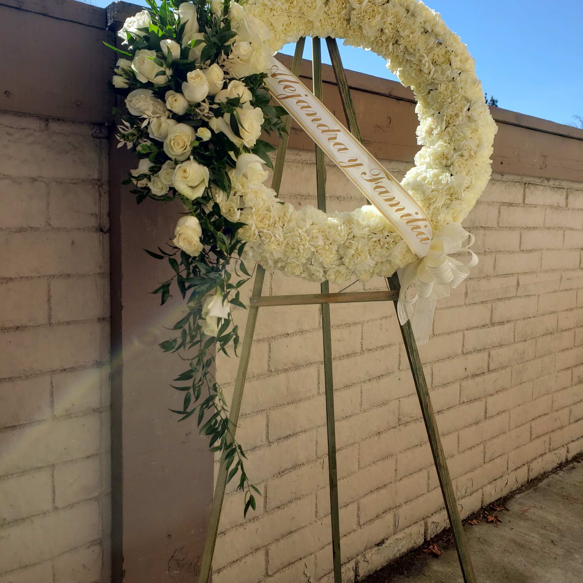 White floral funeral wreath on an easel with roses and ribbon