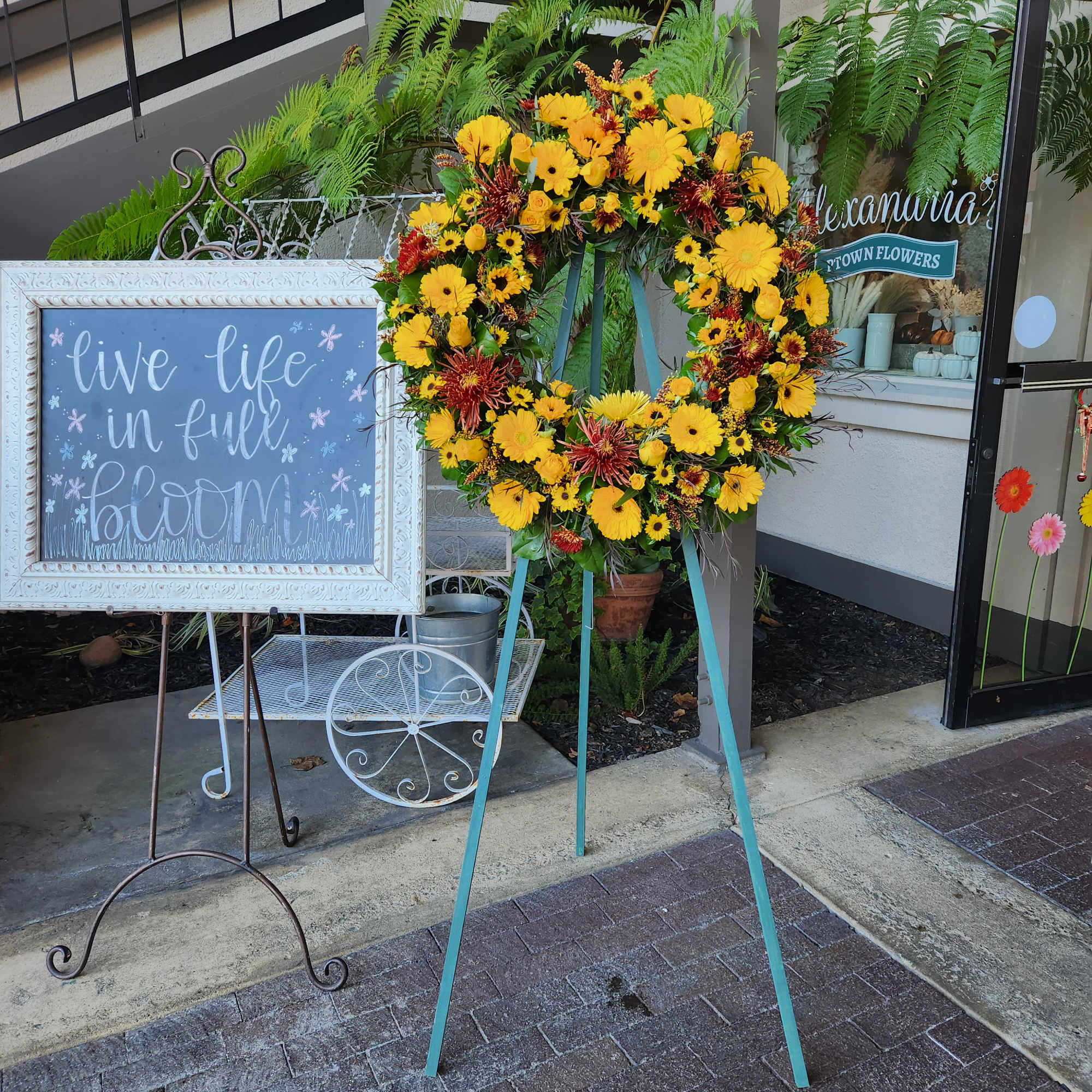 Yellow floral wreath on a stand beside a chalkboard sign