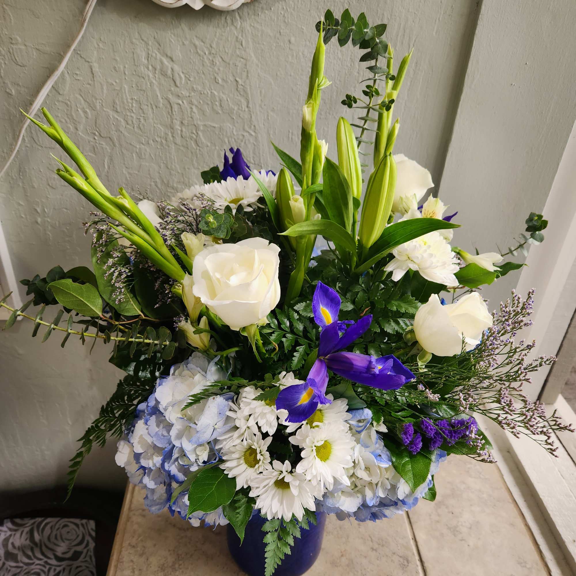 Mixed bouquet with white roses, lilies, irises, and blue hydrangeas in a blue vase