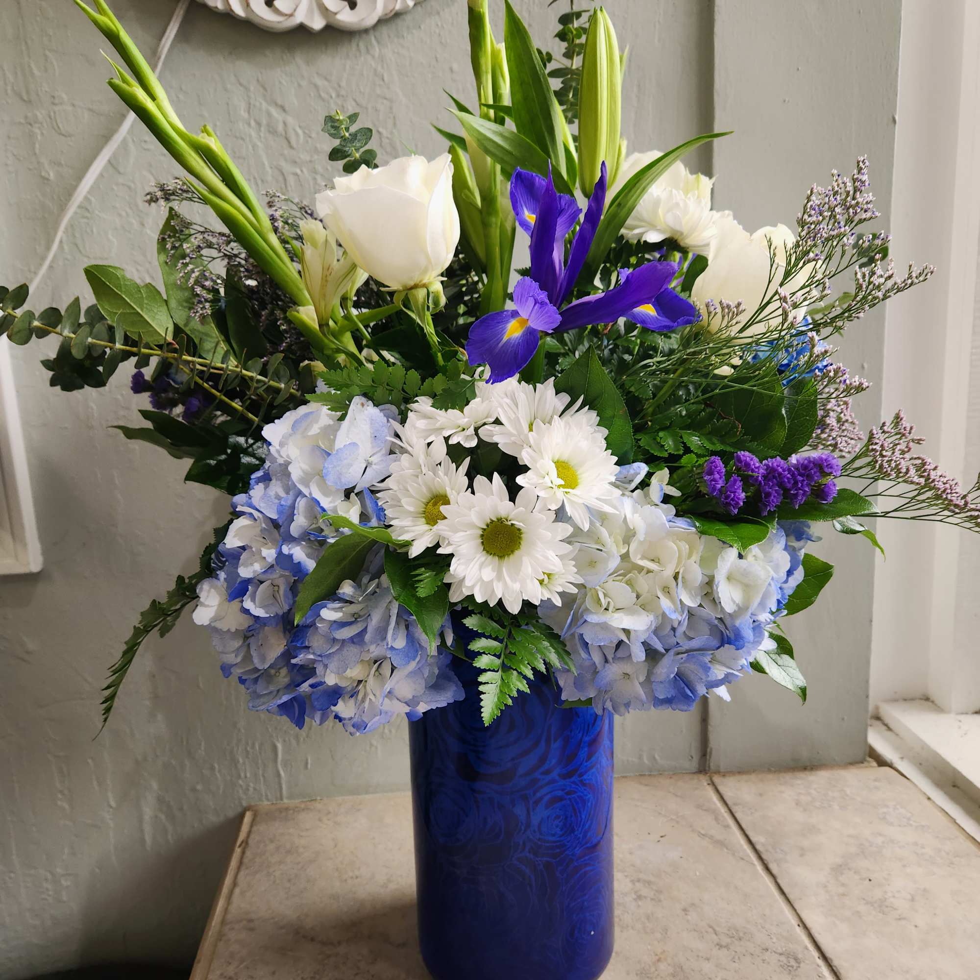 Blue vase arrangement with white lilies, blue irises, and white daisies