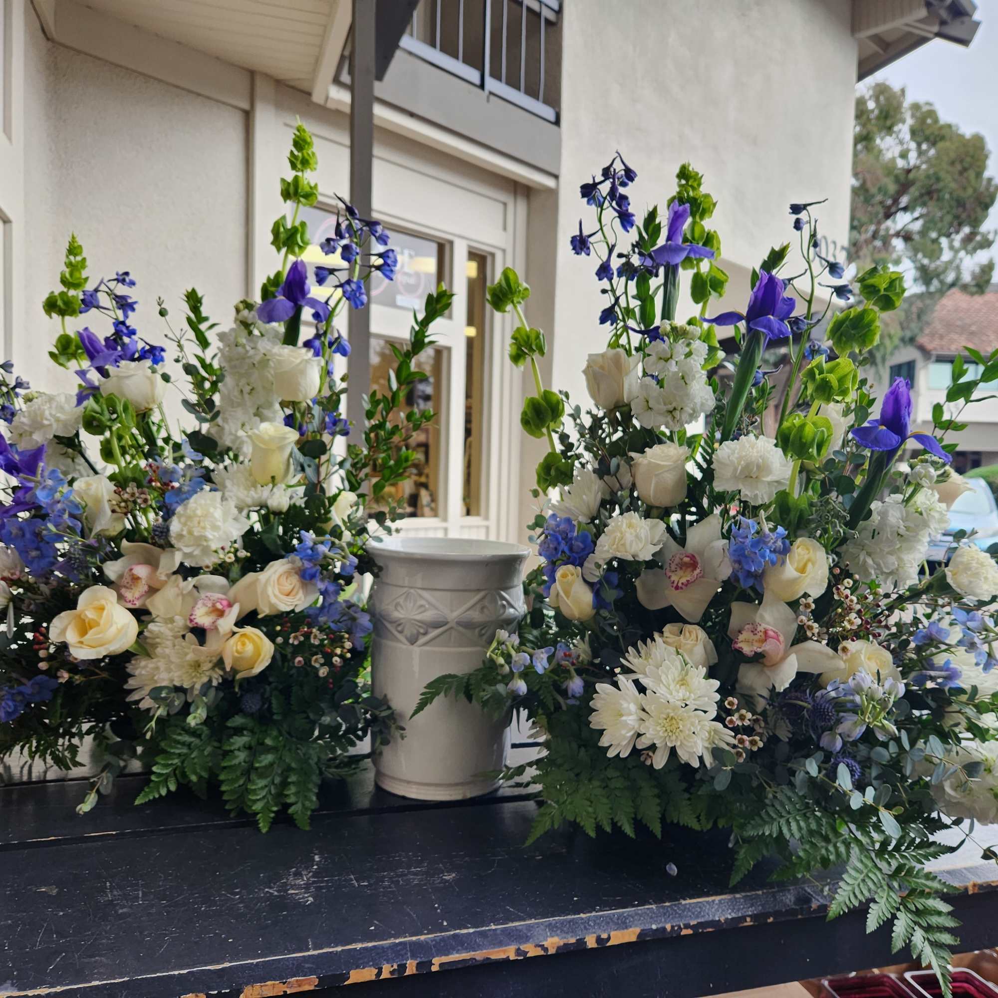 Two large floral arrangements with white, cream, and blue flowers in an outdoor setting.