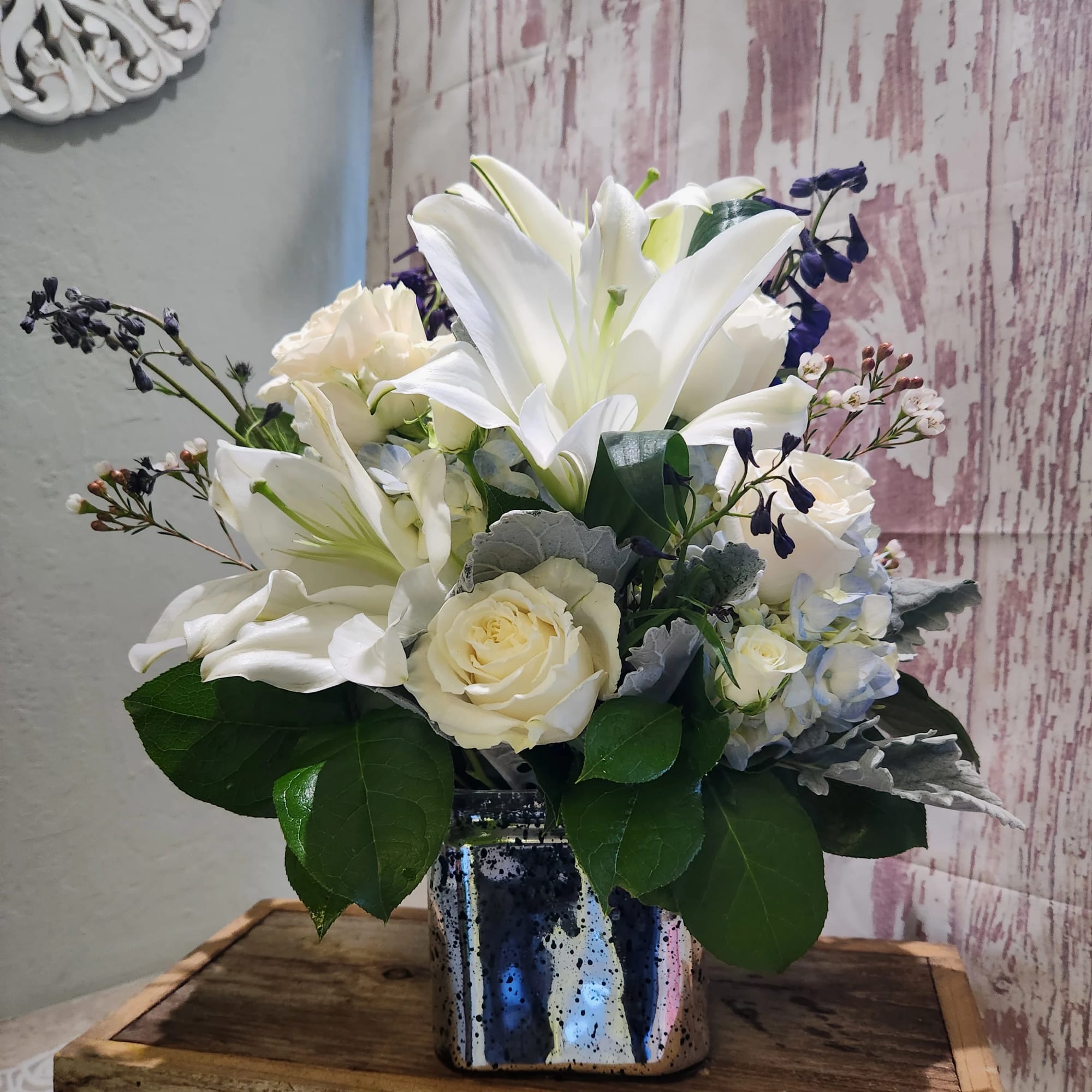 White lilies and roses arranged in a reflective square vase