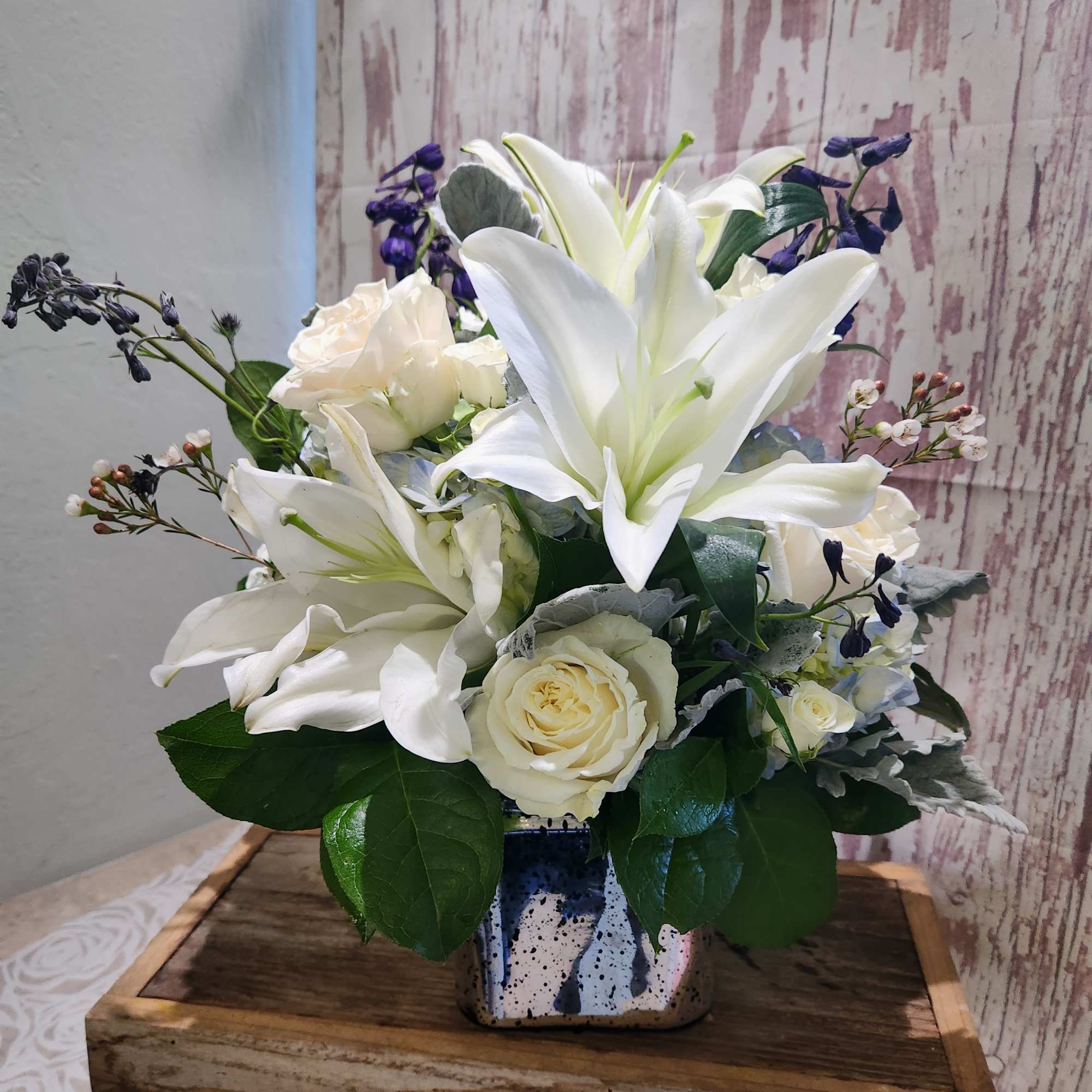White lilies and roses arranged in a small ceramic vase