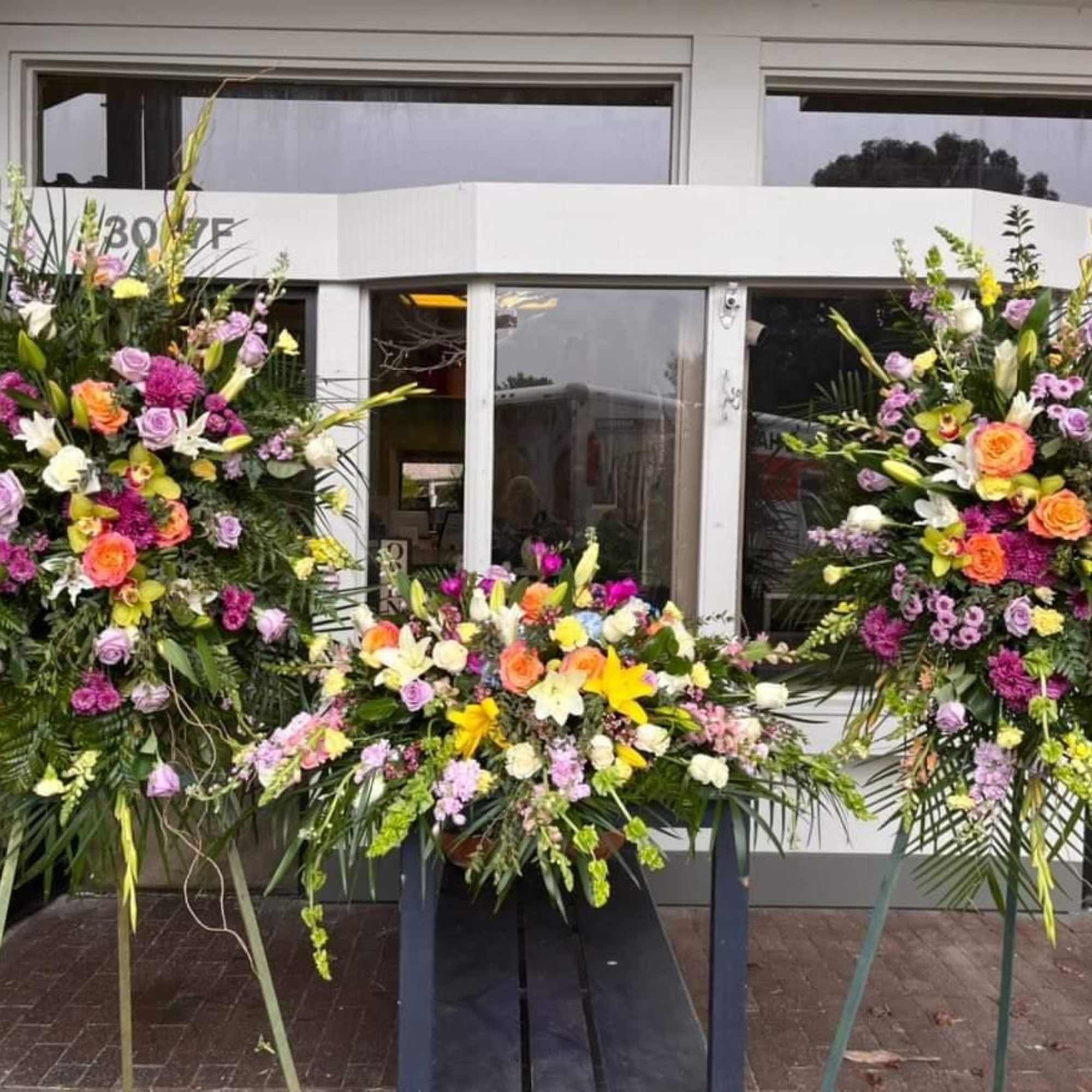 Three large floral standing sprays outside a building entrance