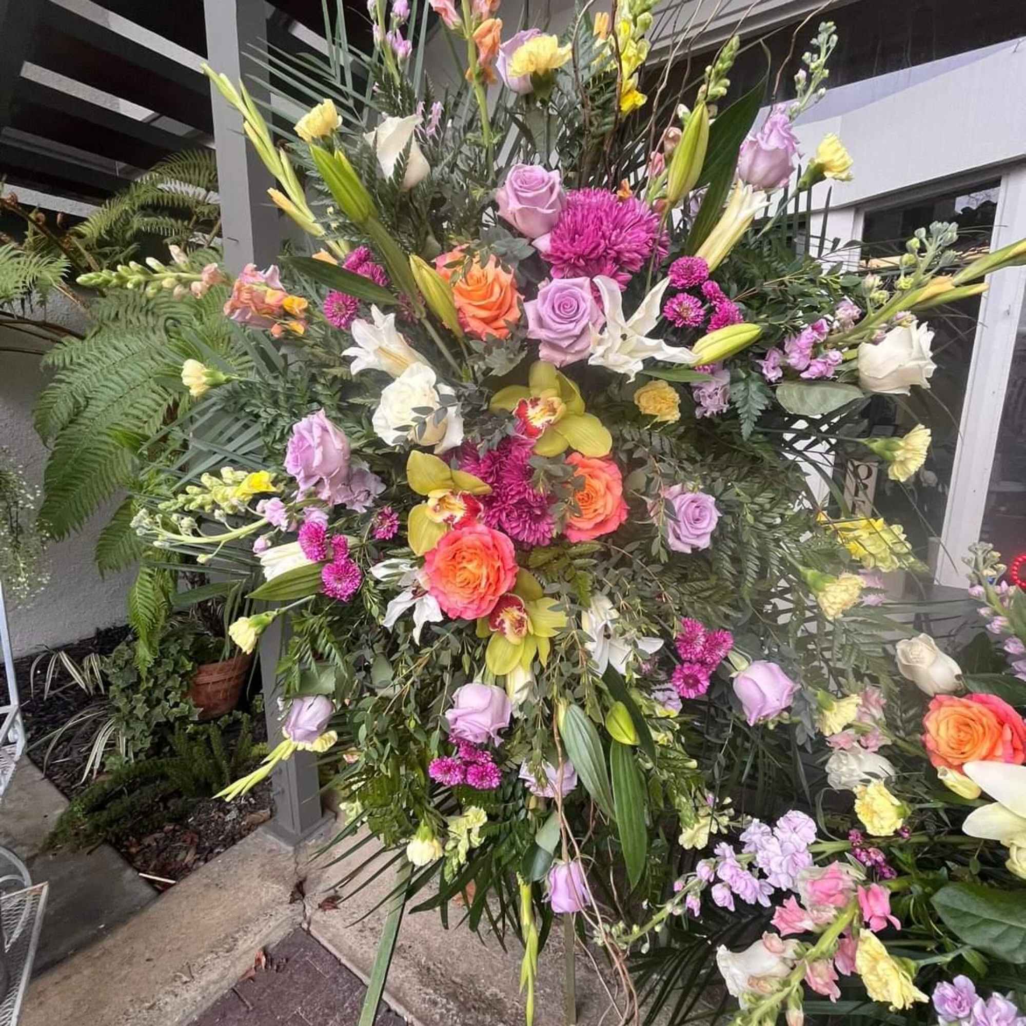 Large standing floral spray with roses, lilies, and orchids in pink, yellow, and white