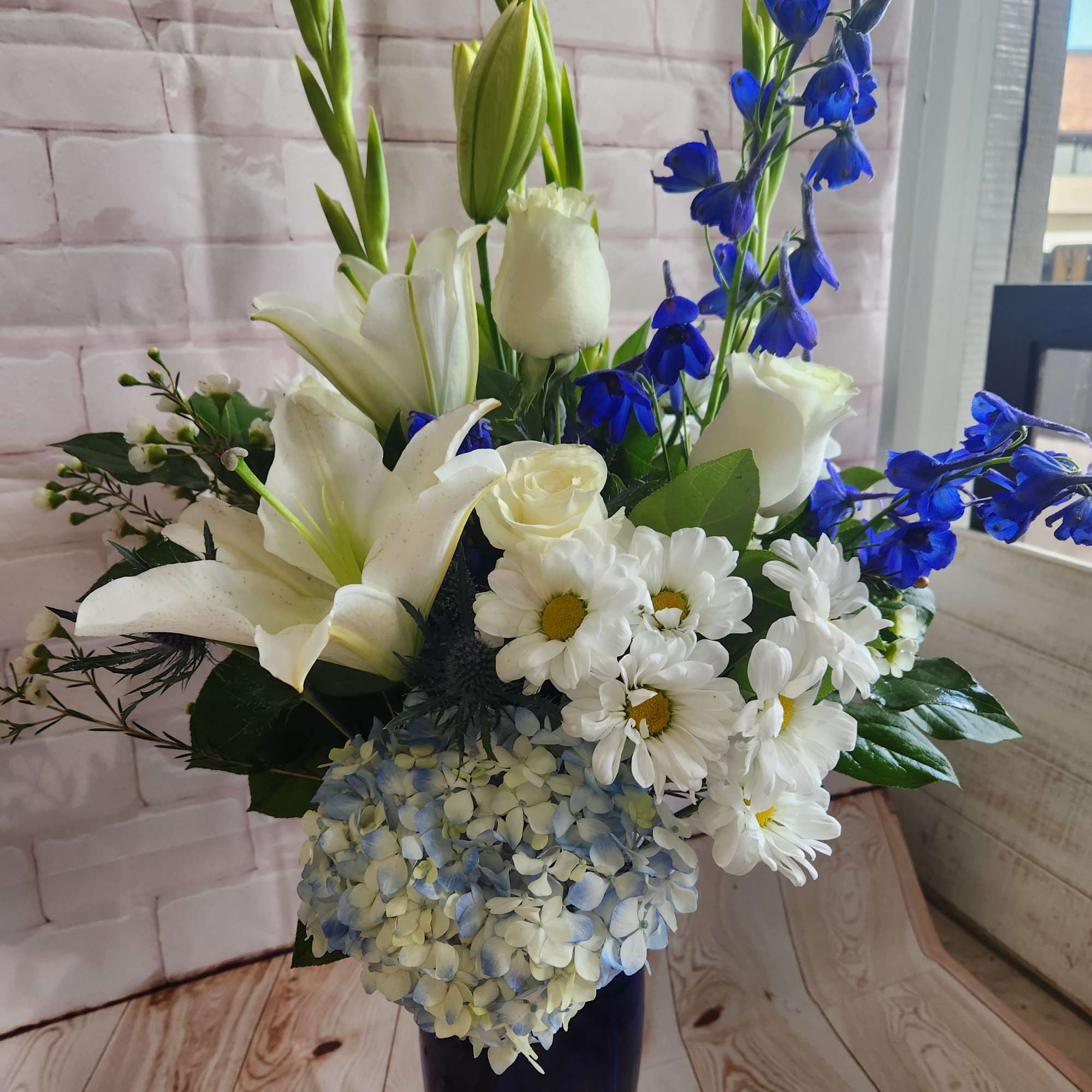 White lilies, roses, daisies, and blue flowers in a tall vase