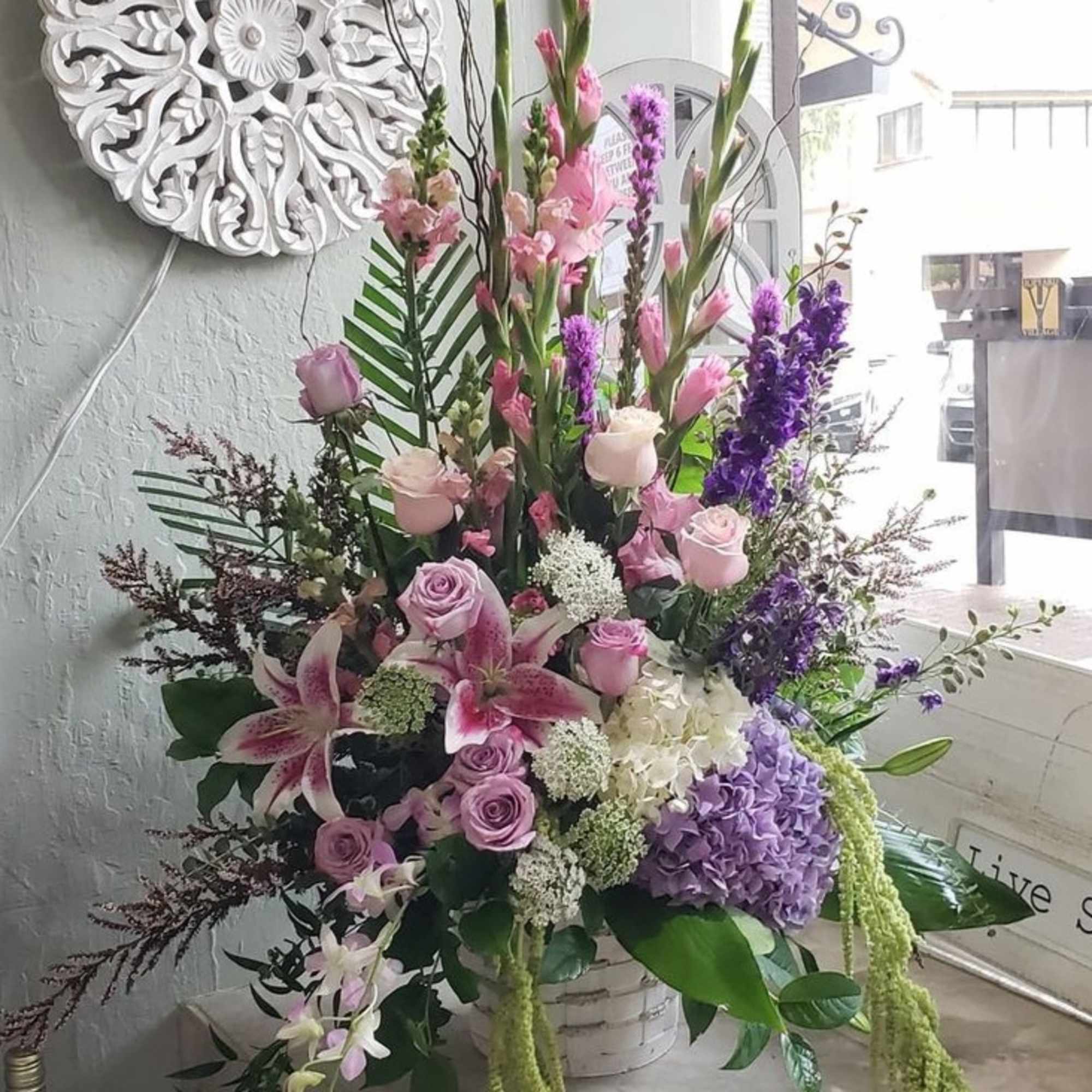 Tall floral arrangement with pink roses, lilies, and purple blooms in a white basket