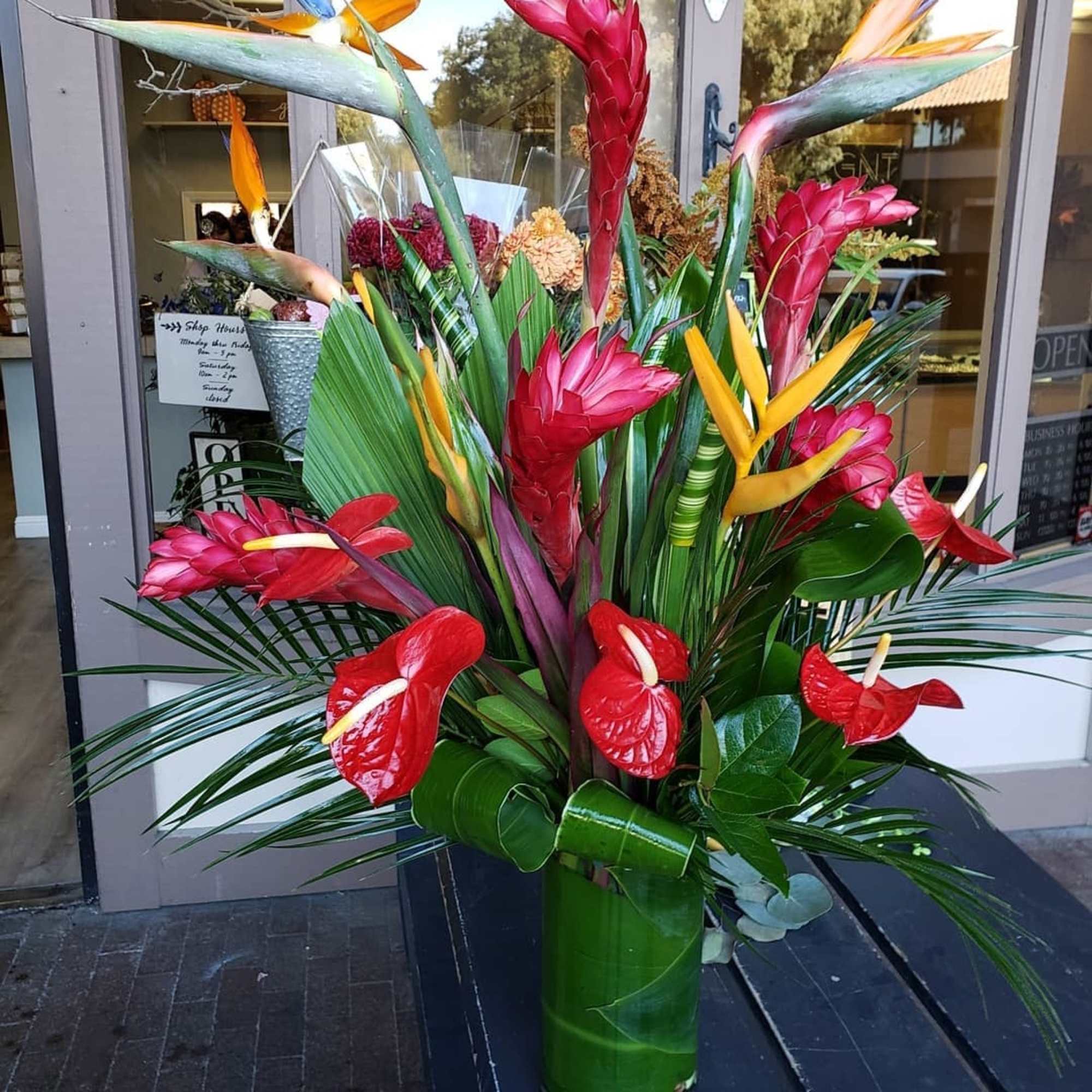 Tropical arrangement with red ginger, bird of paradise, and anthuriums in a tall vase