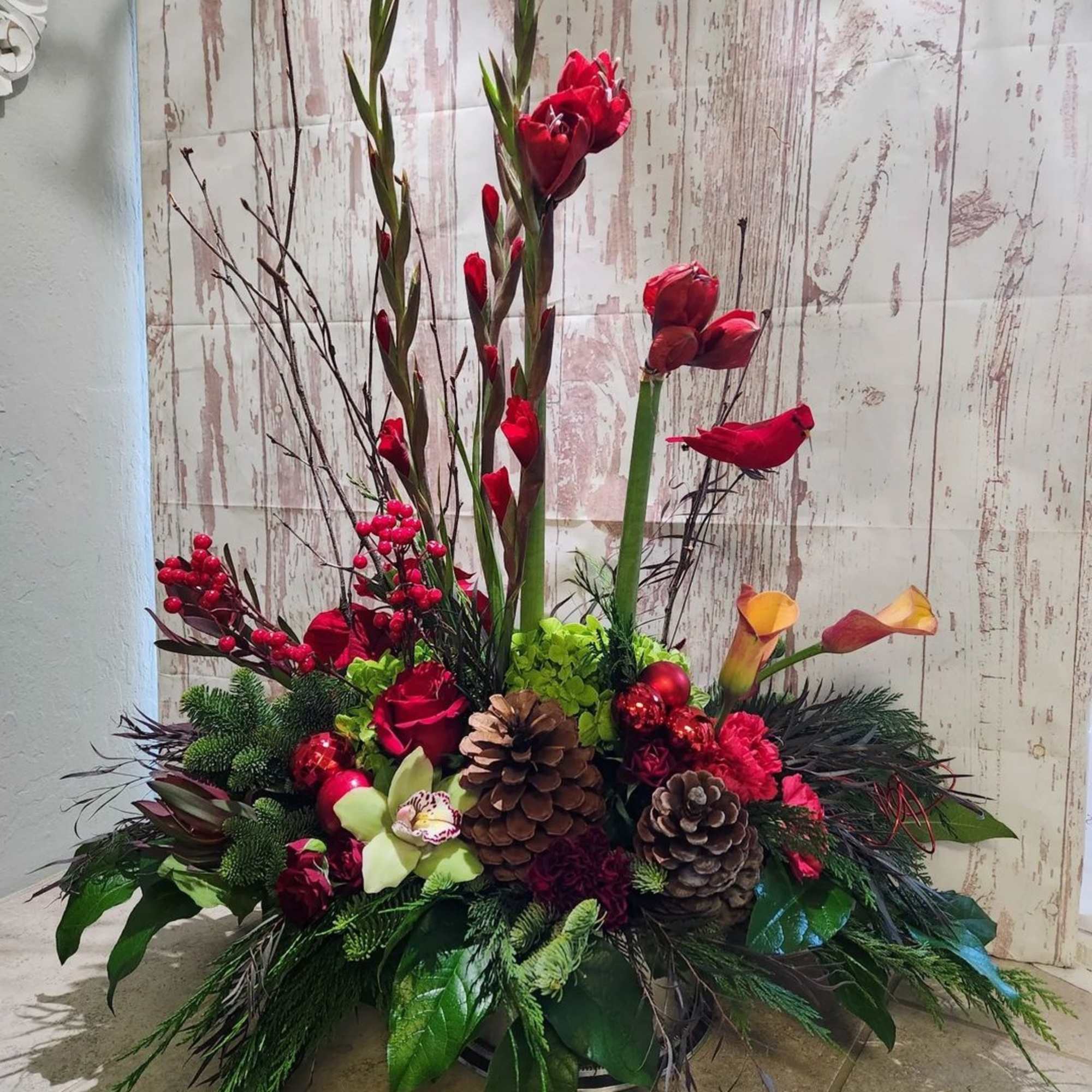 Red floral arrangement with pinecones and calla lilies in a low container