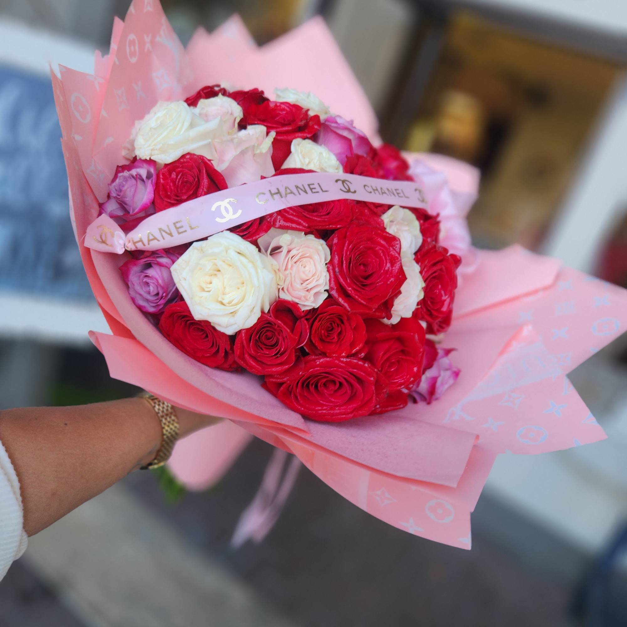 Handheld bouquet of red, white, and pink roses wrapped in pink paper