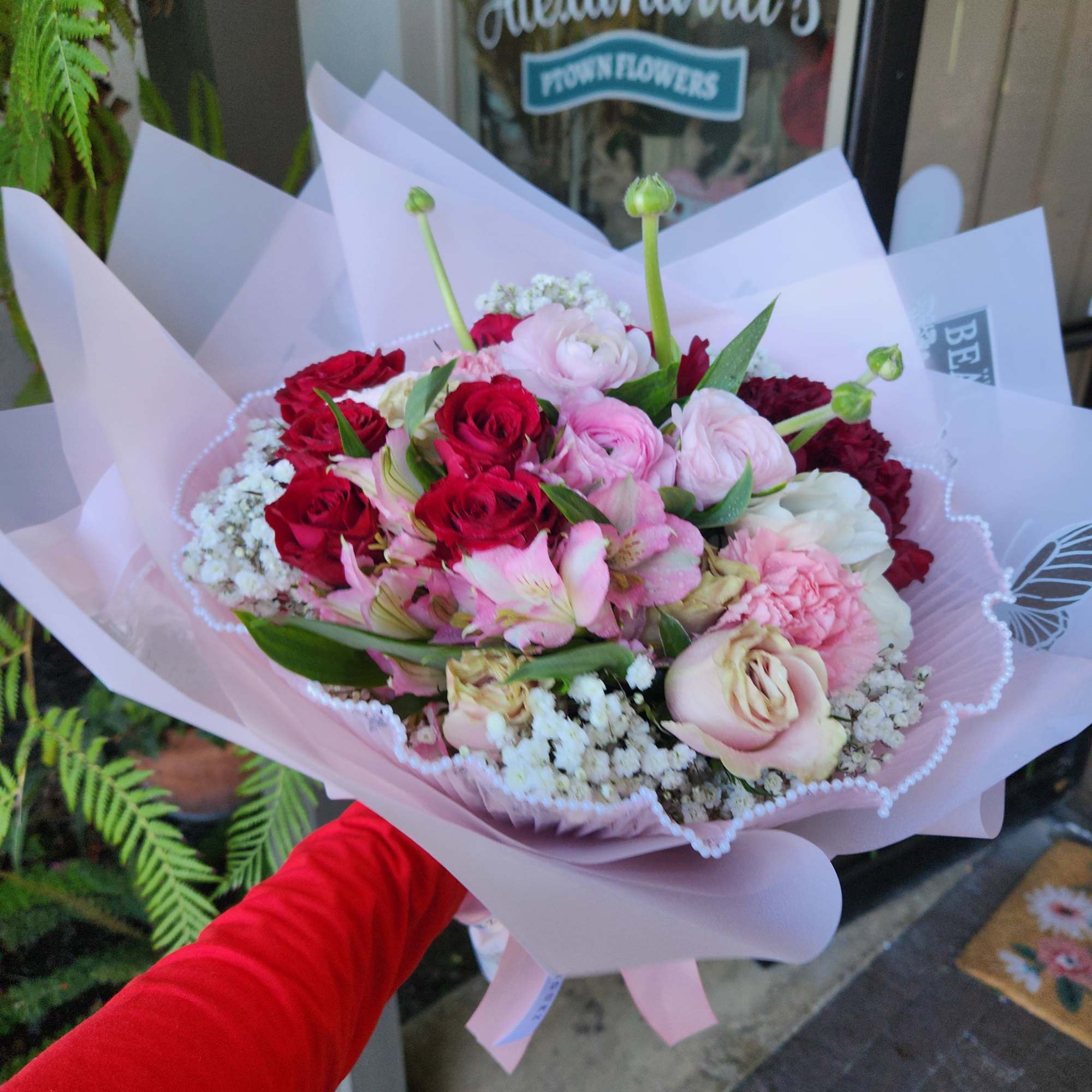Handheld bouquet of pink and red roses wrapped in pale pink paper