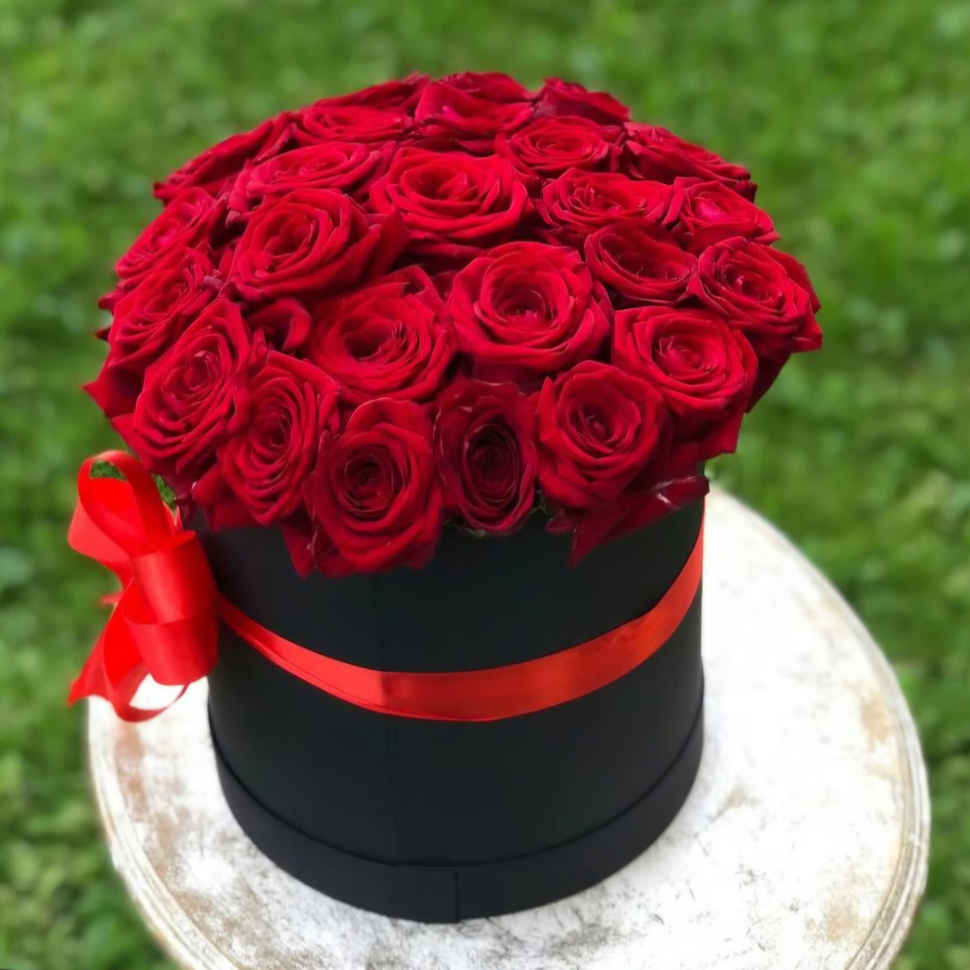 Red roses arranged in a black round box with a red ribbon