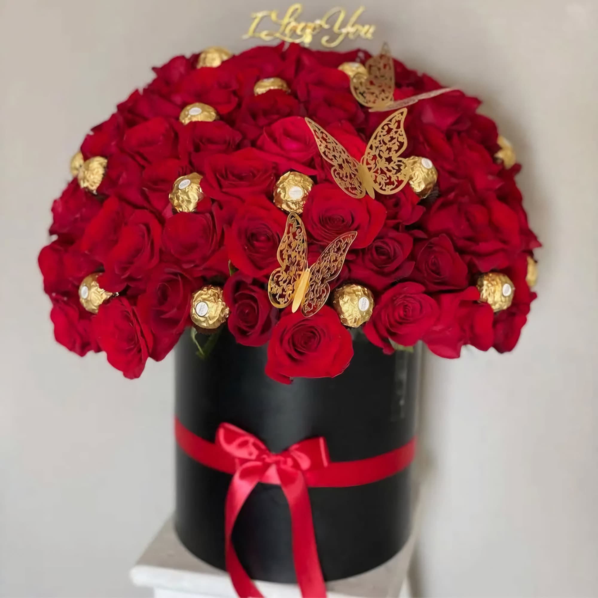 Red roses in a black hatbox with gold butterfly accents and a red ribbon