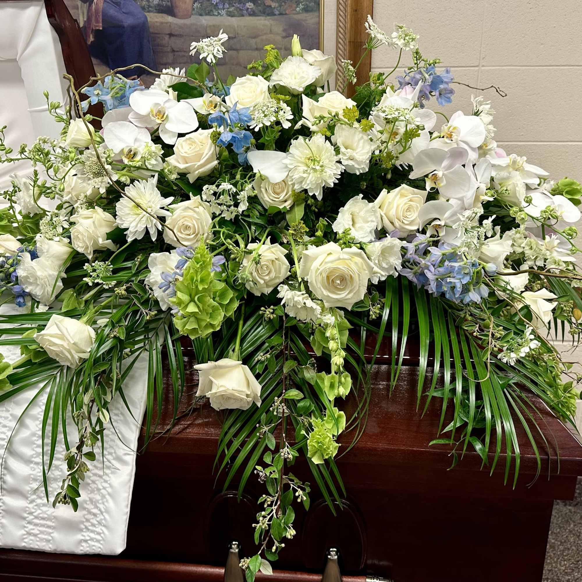 White floral casket spray with orchids, roses, and blue accents