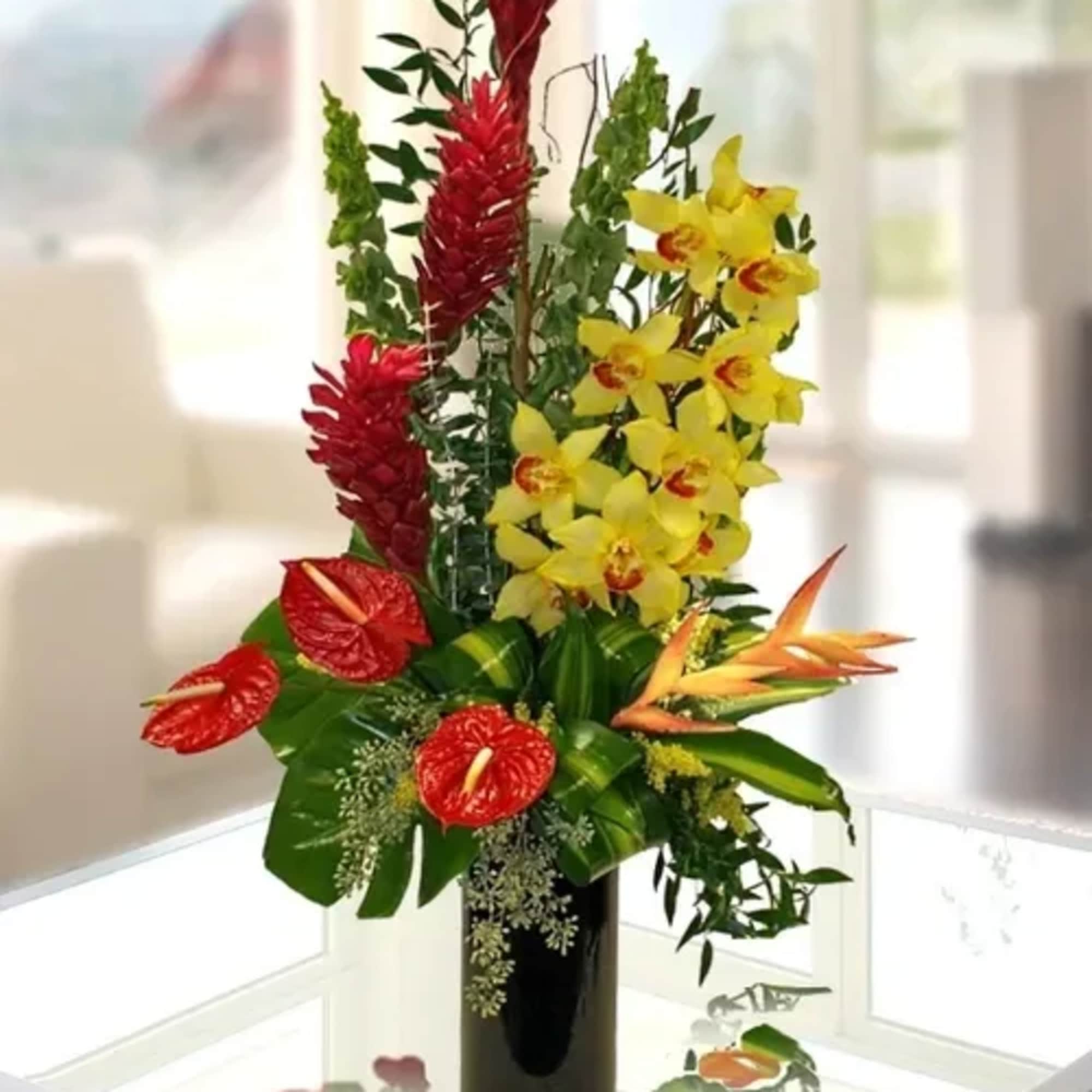 Tropical flower arrangement with red anthuriums, yellow orchids, and orange bird-of-paradise in a black vase