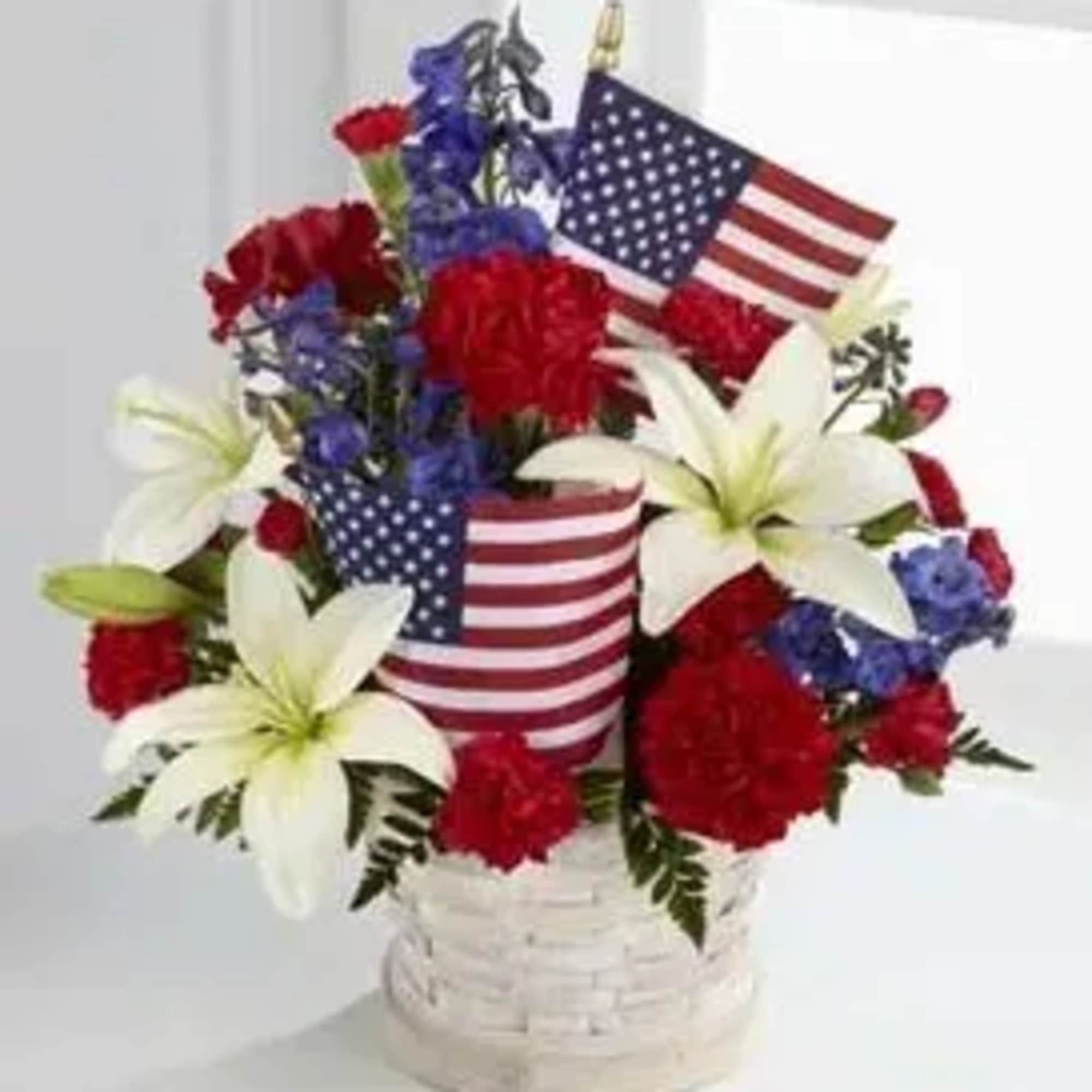Red, white, and blue floral arrangement in a white basket with American flags