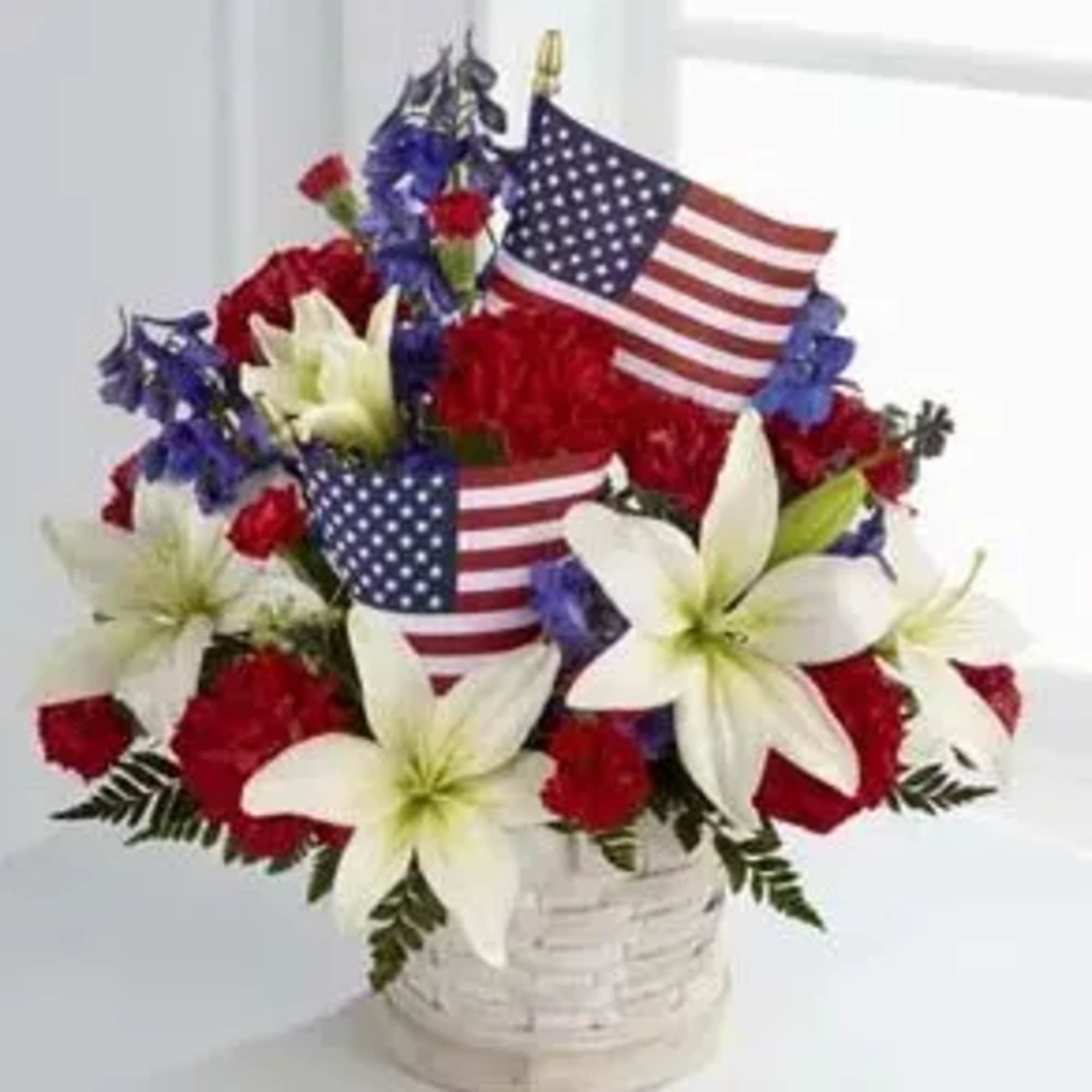 Red, white, and blue flower arrangement with American flags in a white basket