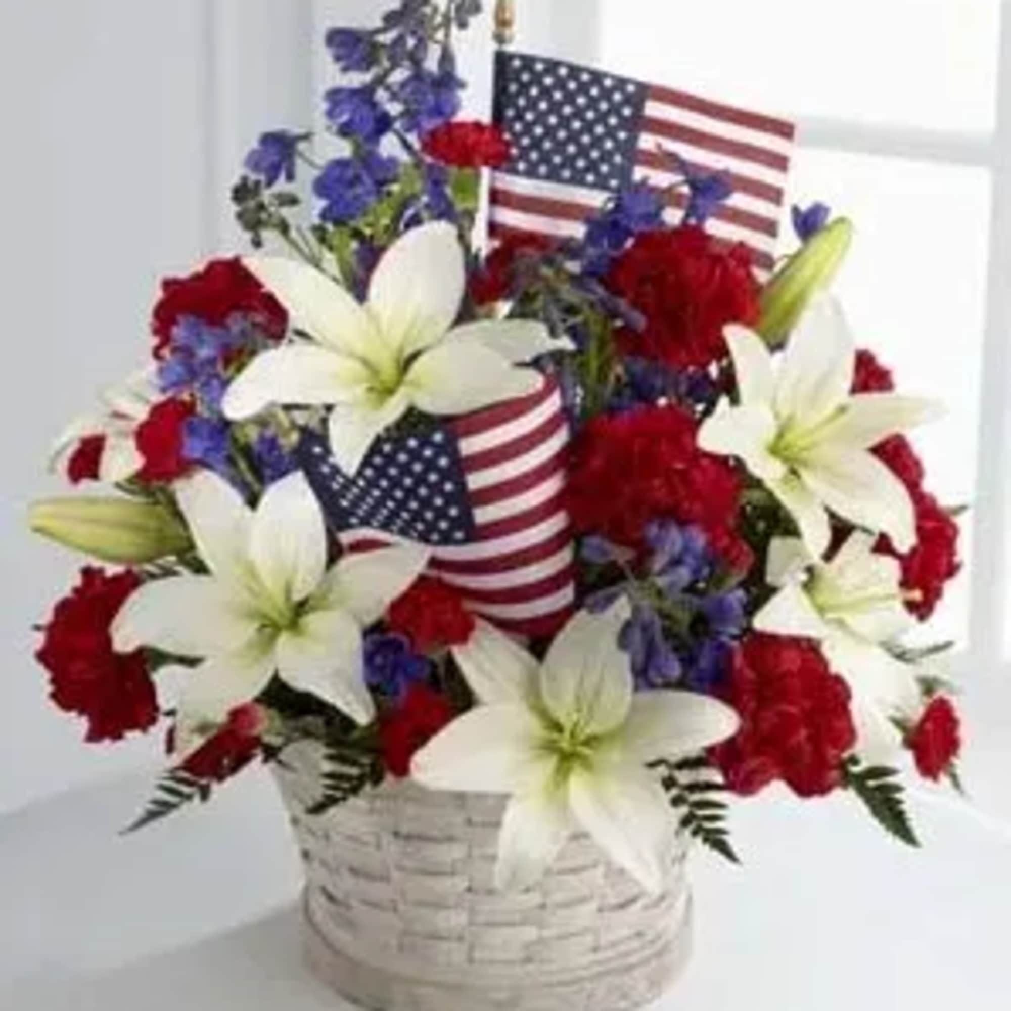 Basket arrangement of red, white, and blue flowers with small American flags