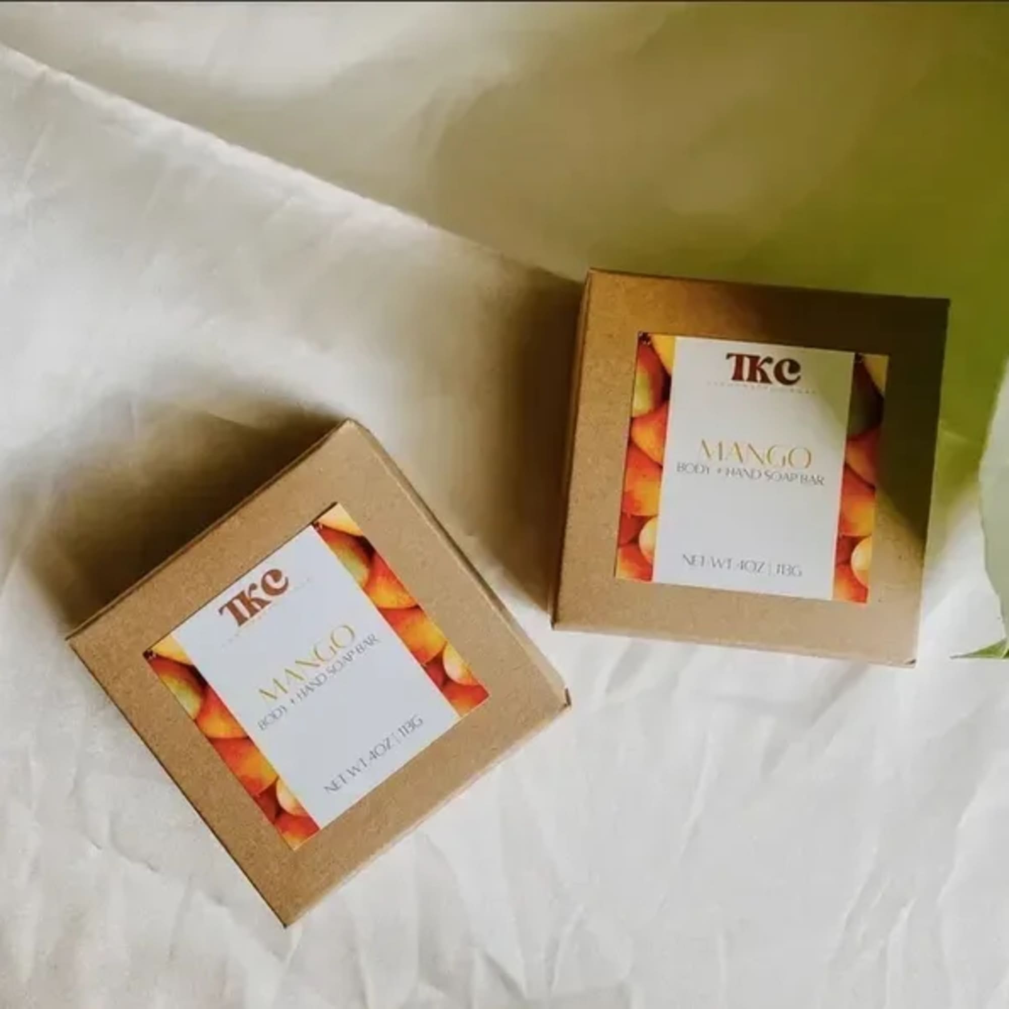 Two boxed mango body and hand soap bars on white fabric