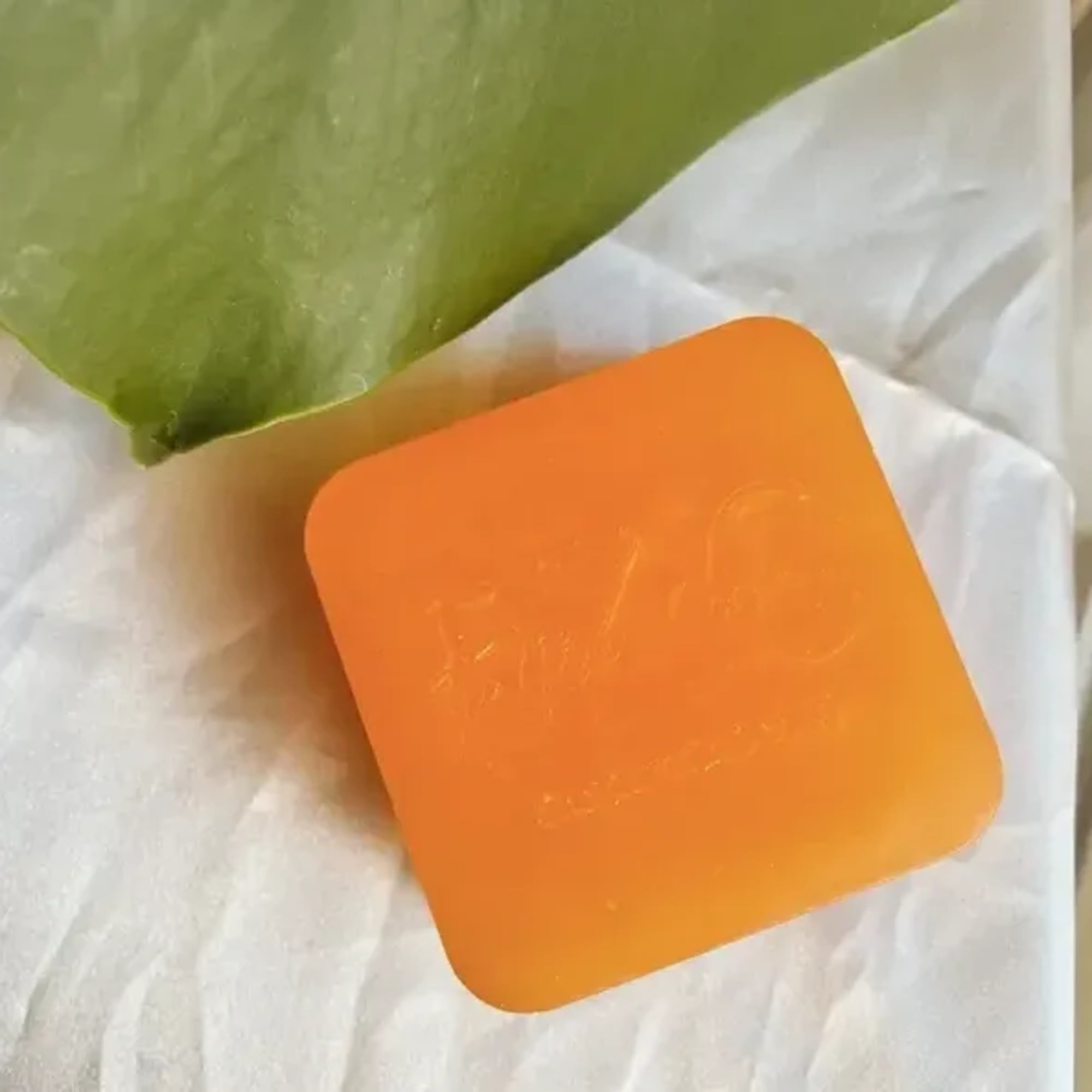 Orange square soap bar on white tissue with a green wrapper
