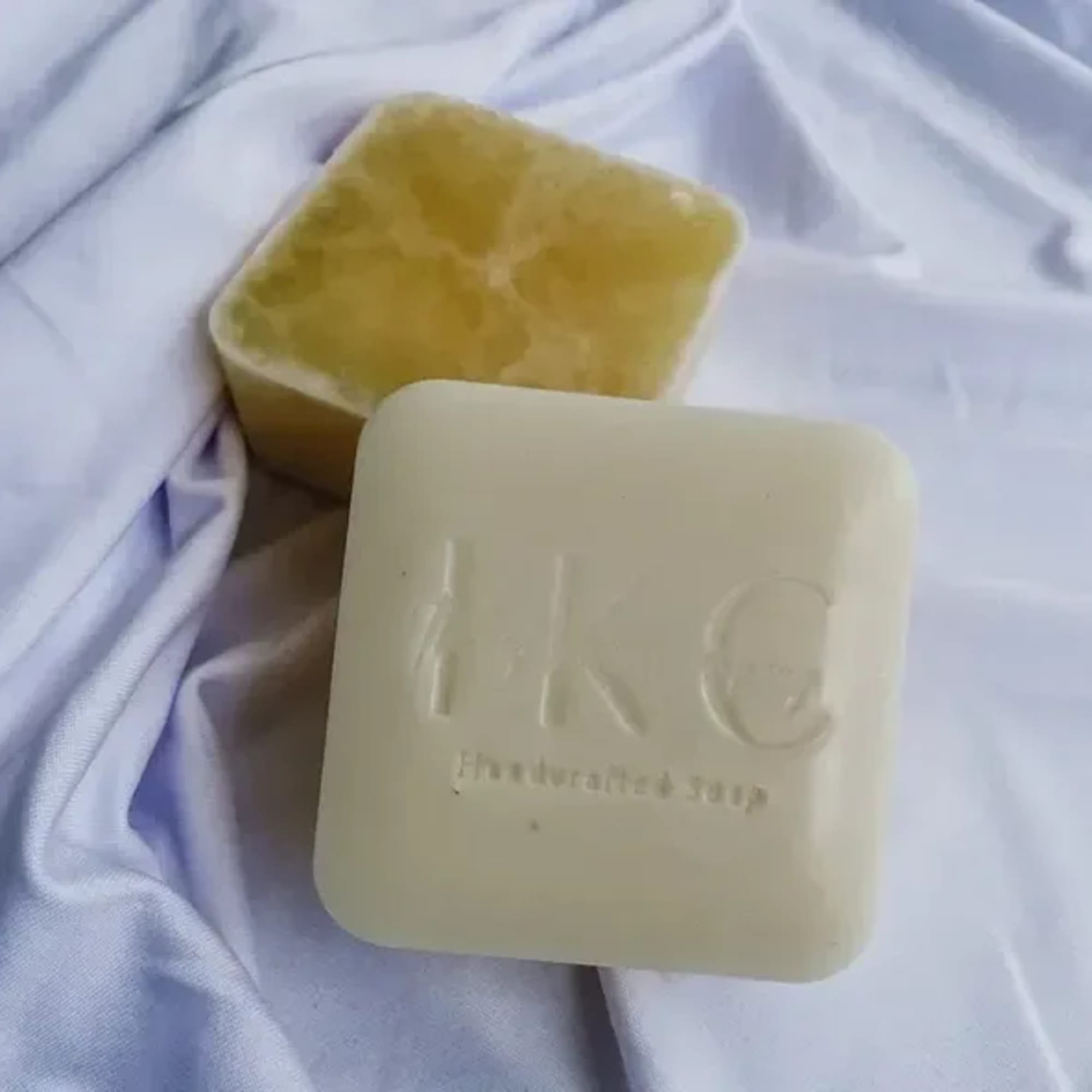 Two square bars of soap on white fabric, one cut open to show yellow interior