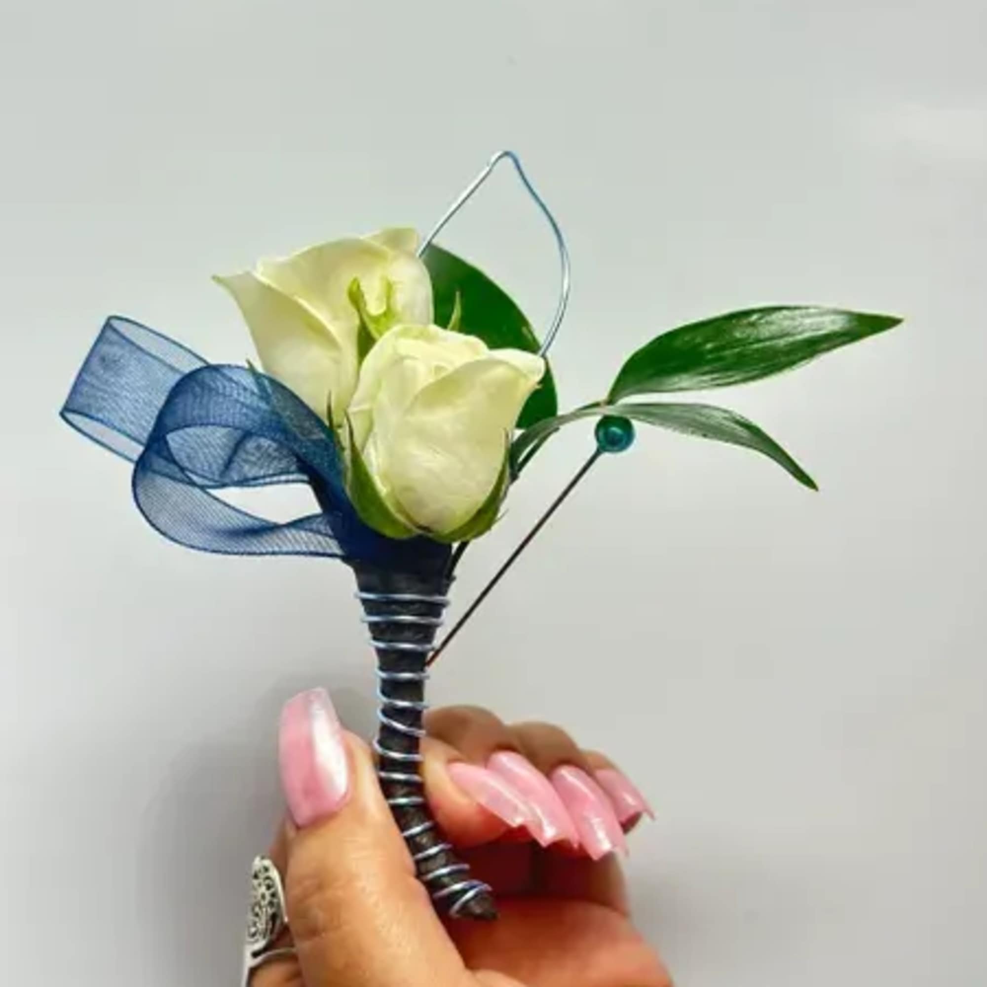 Small white calla lily boutonniere with blue ribbon and green leaves