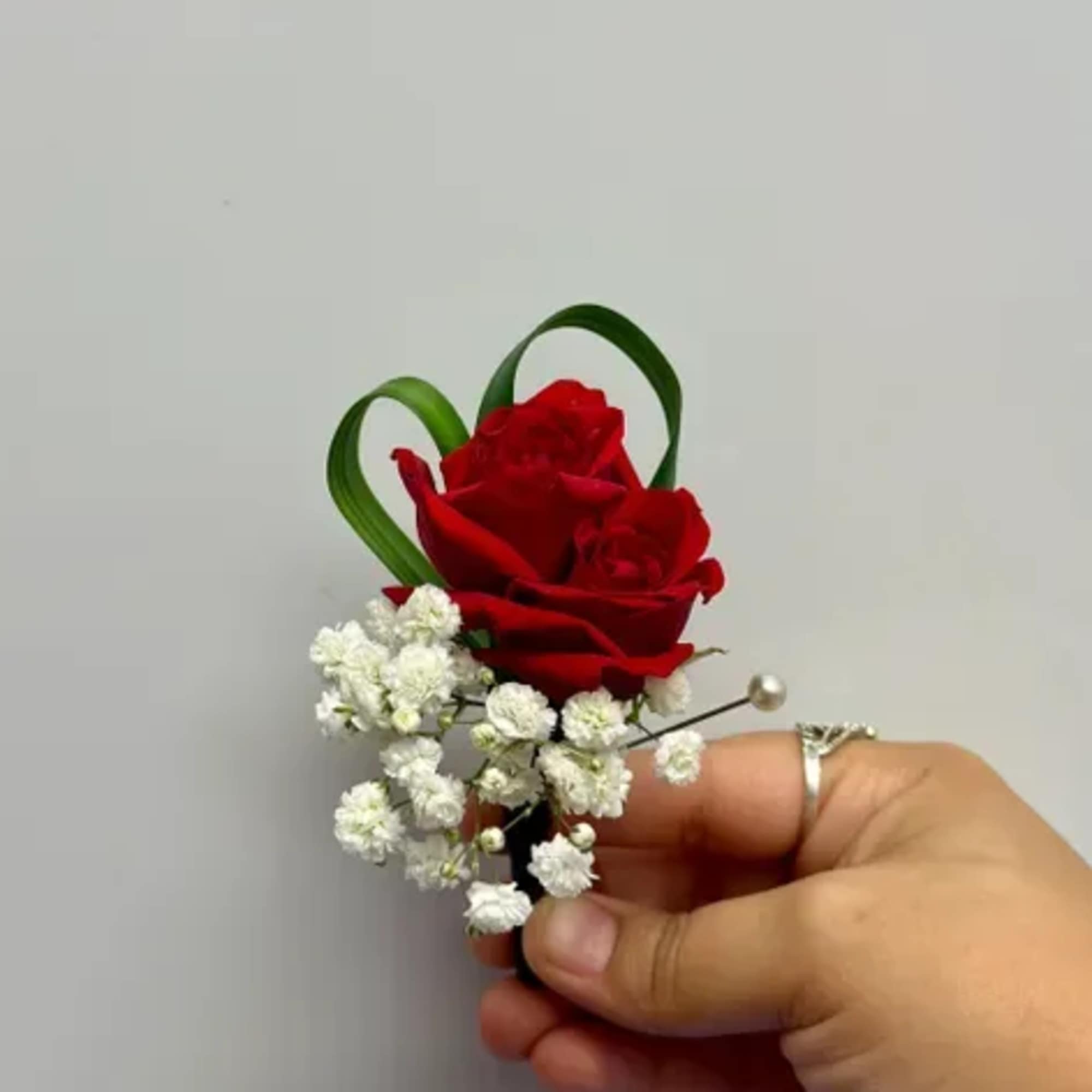 Red rose boutonniere with white baby's breath and green loops