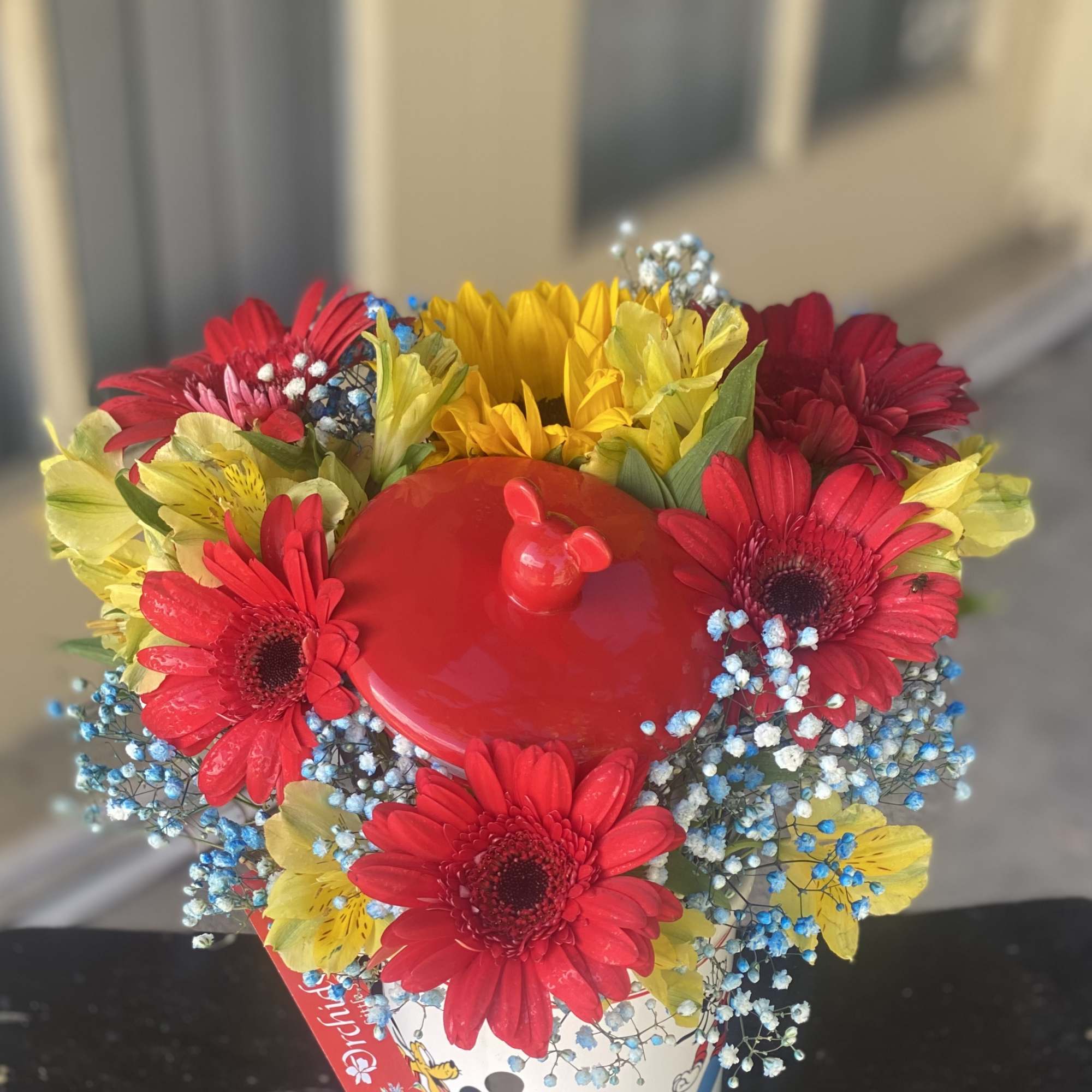 Bright mixed bouquet in a Mickey Mouse bucket with red, yellow, and blue flowers