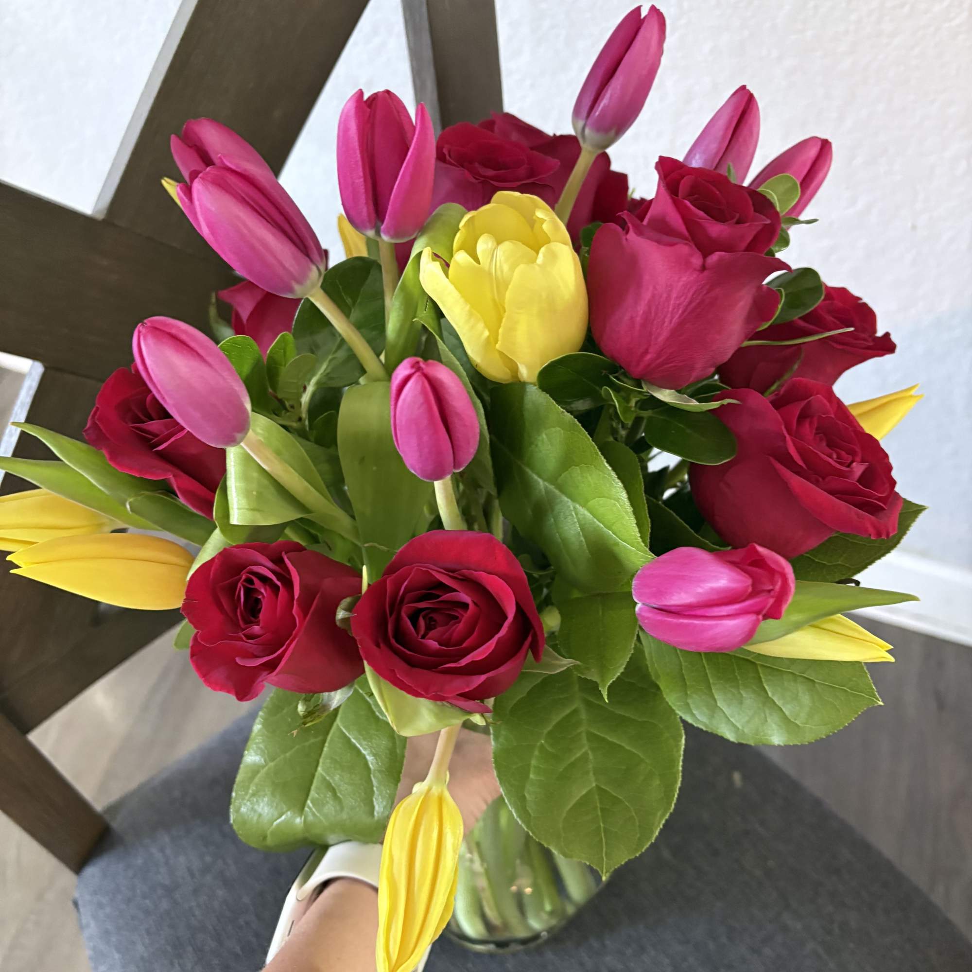 Bouquet of pink tulips, yellow tulips, and red roses in a glass vase