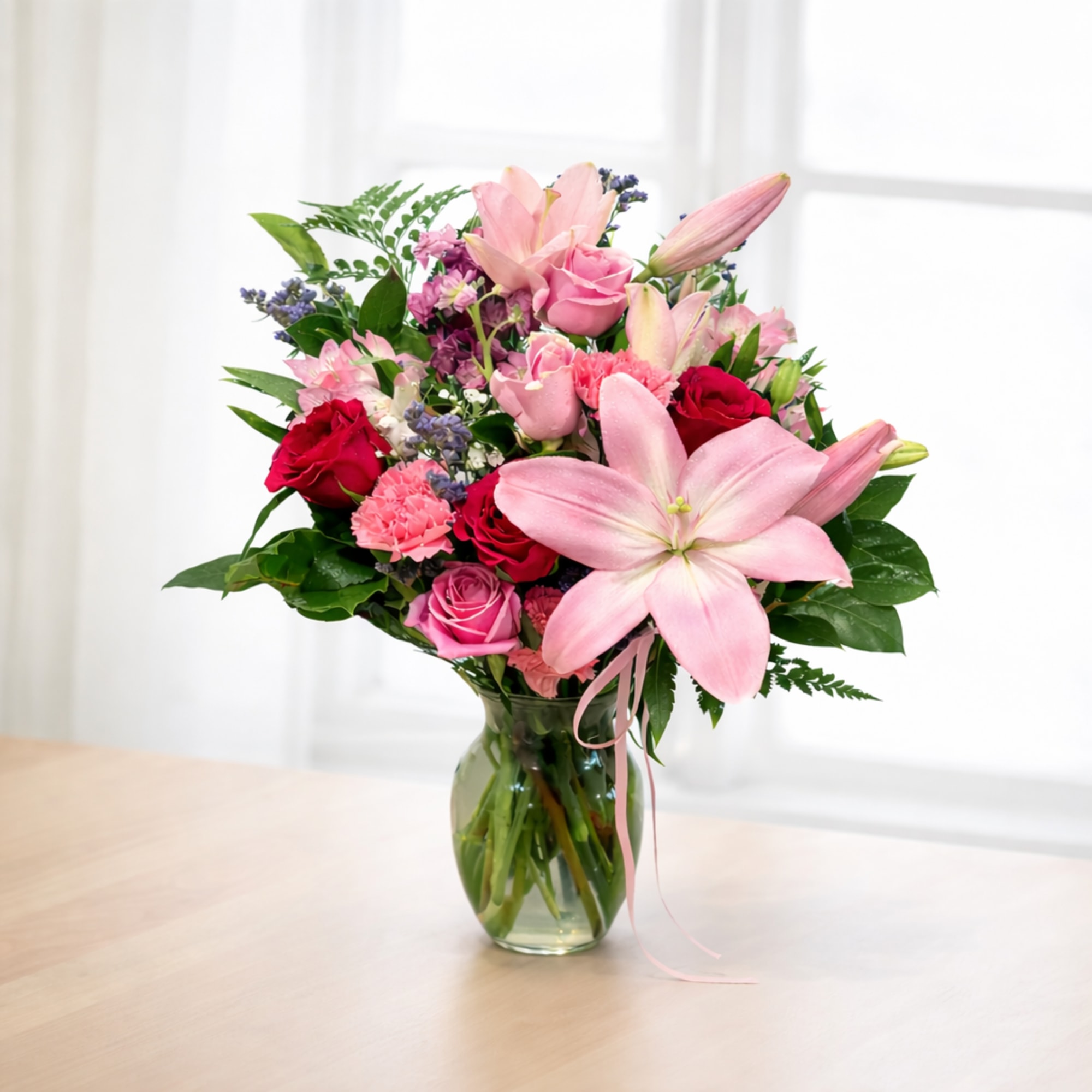 Pink lilies and roses arranged in a glass vase