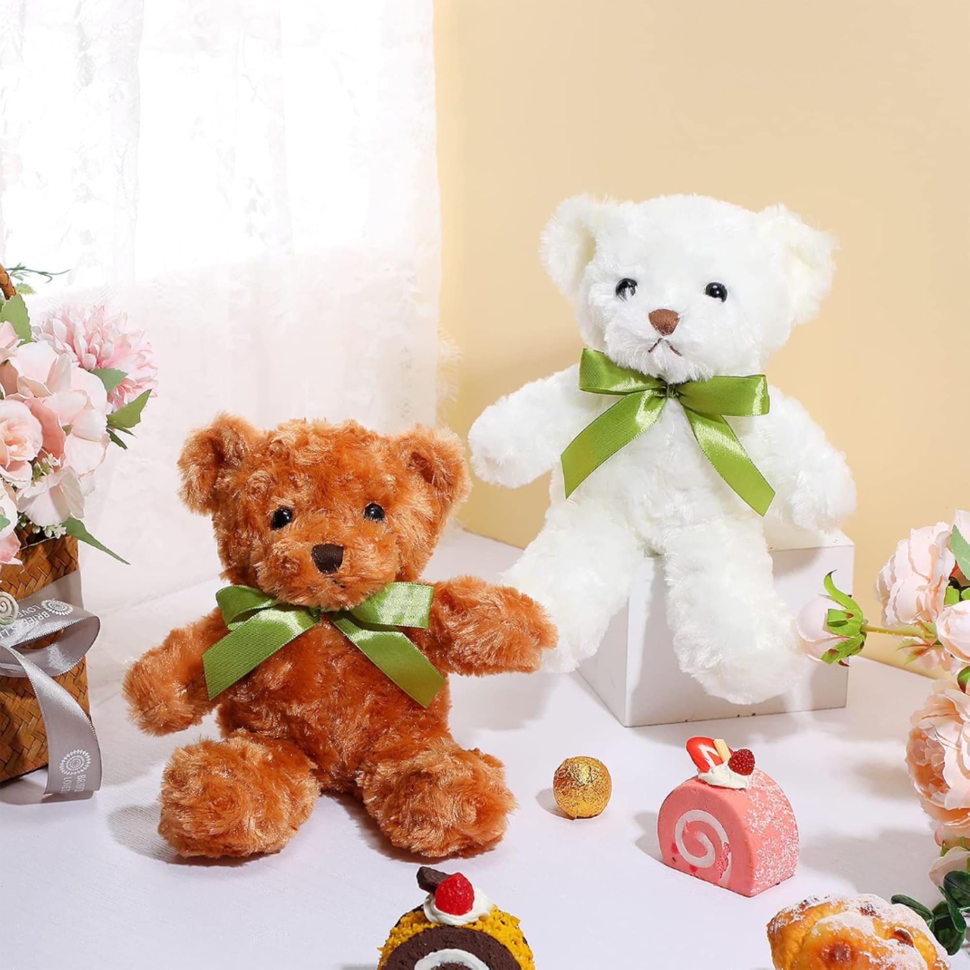 Two teddy bears with green bows beside pink flowers and small candies