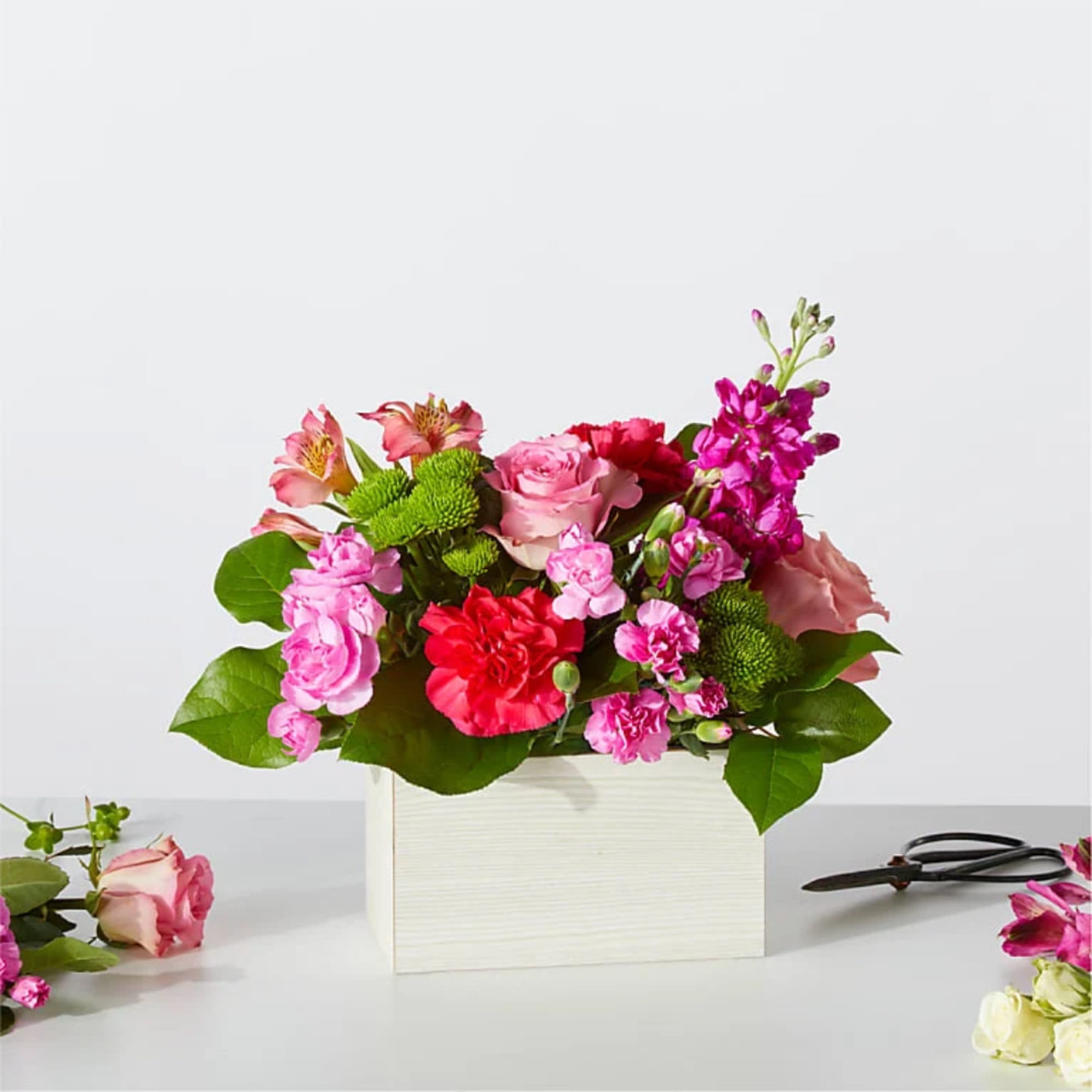 Pink and red flower arrangement in a white box with green foliage