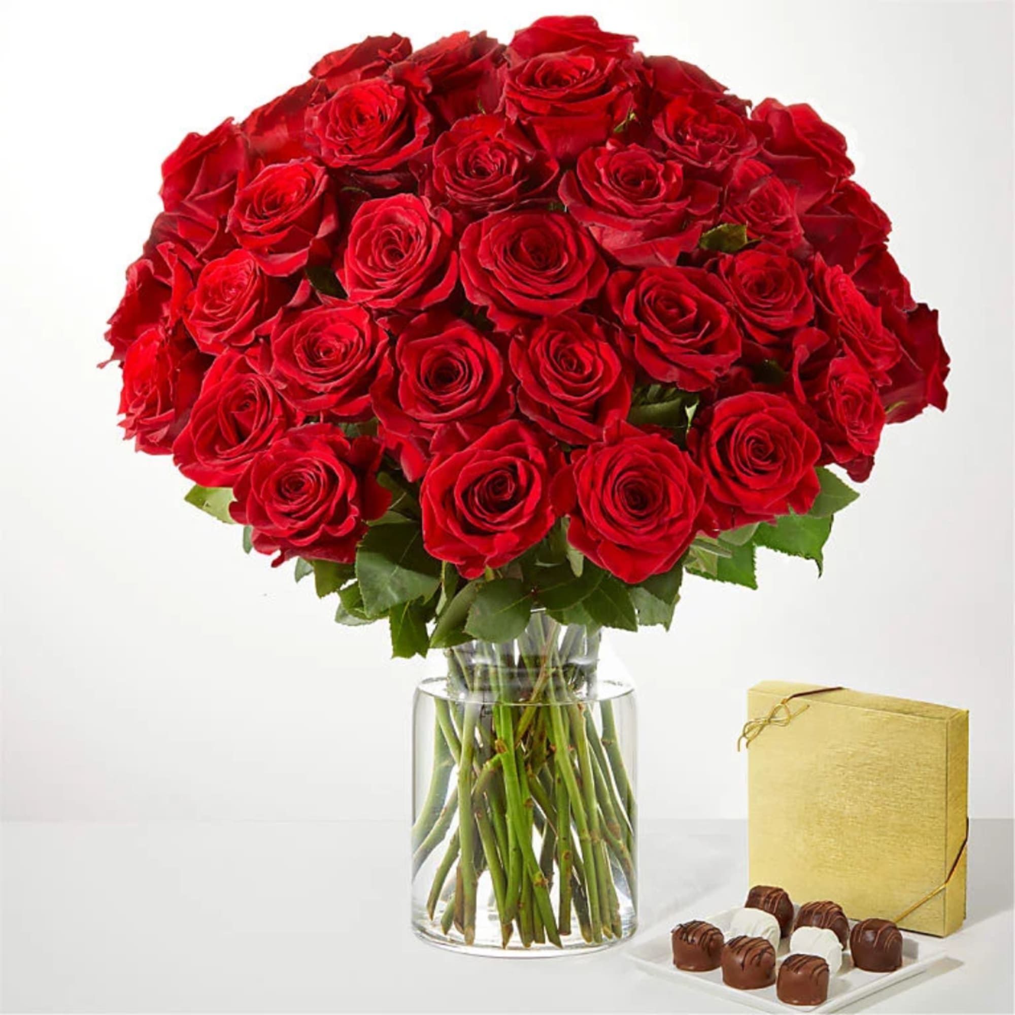 Red rose bouquet in a clear glass vase with a gold gift box and chocolates