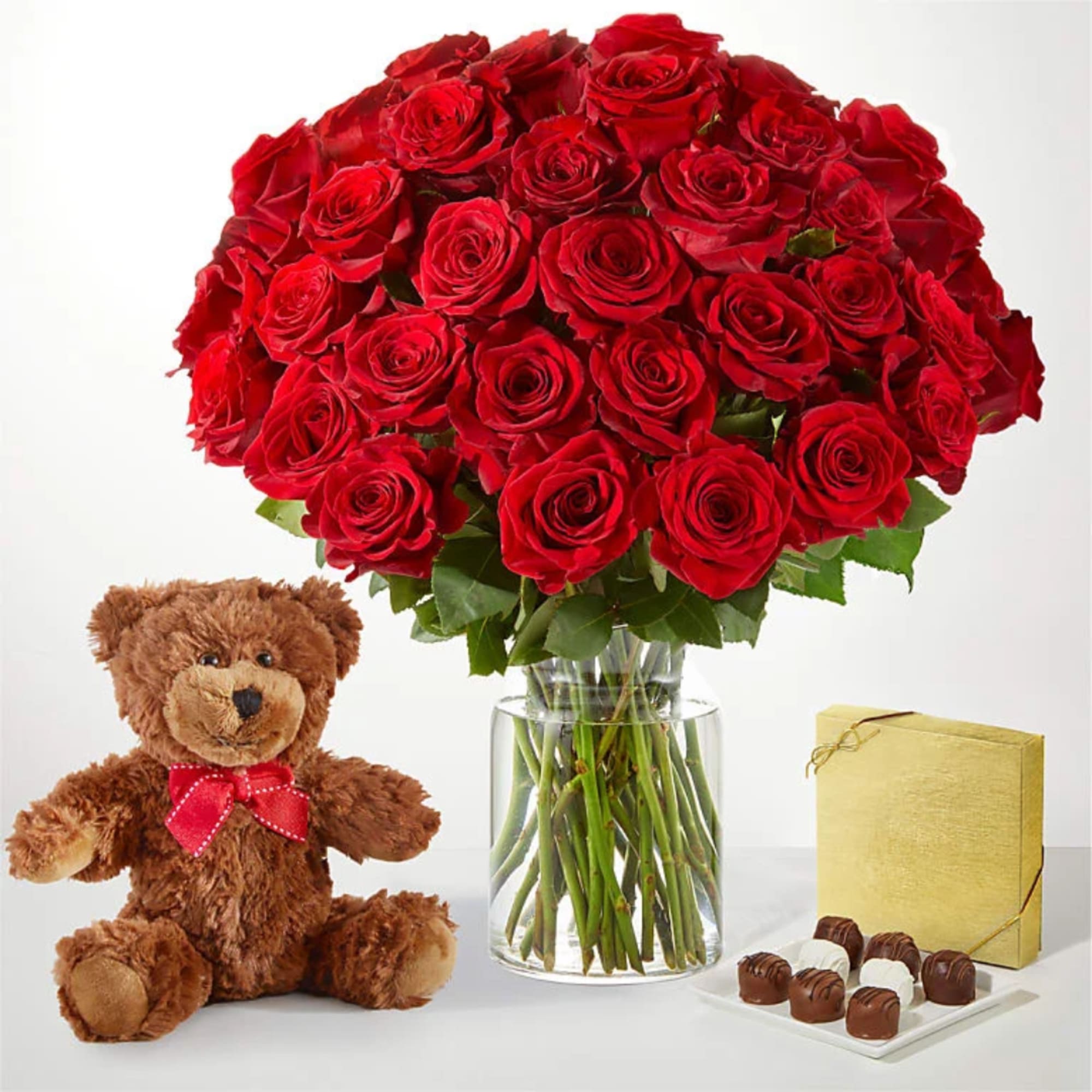 Red rose bouquet in a glass vase with a teddy bear and chocolates